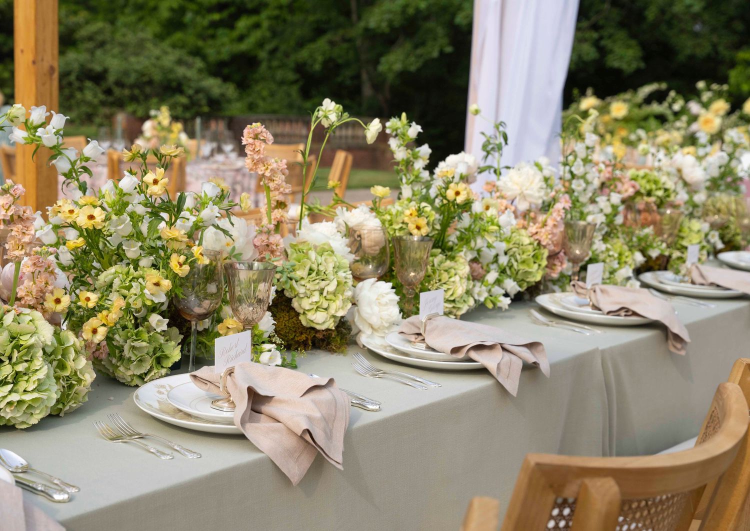Elegant wedding reception table decorated with blush pink and white floral arrangements, crystal glassware and natural wood chairs.