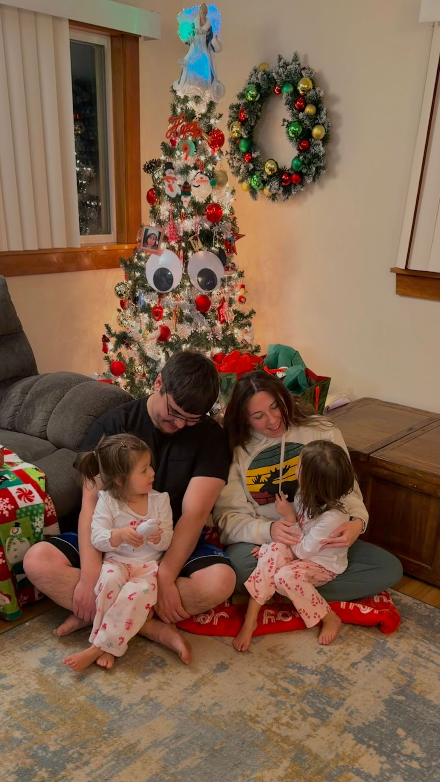 Family gathering around a decorated Christmas tree with matching pajamas on a patterned rug.