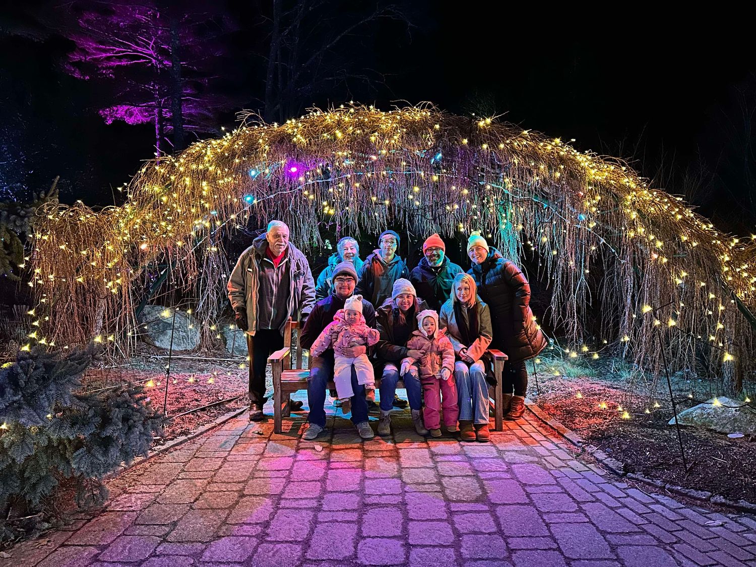 Nighttime group photo under illuminated purple and gold lights along a garden pathway.