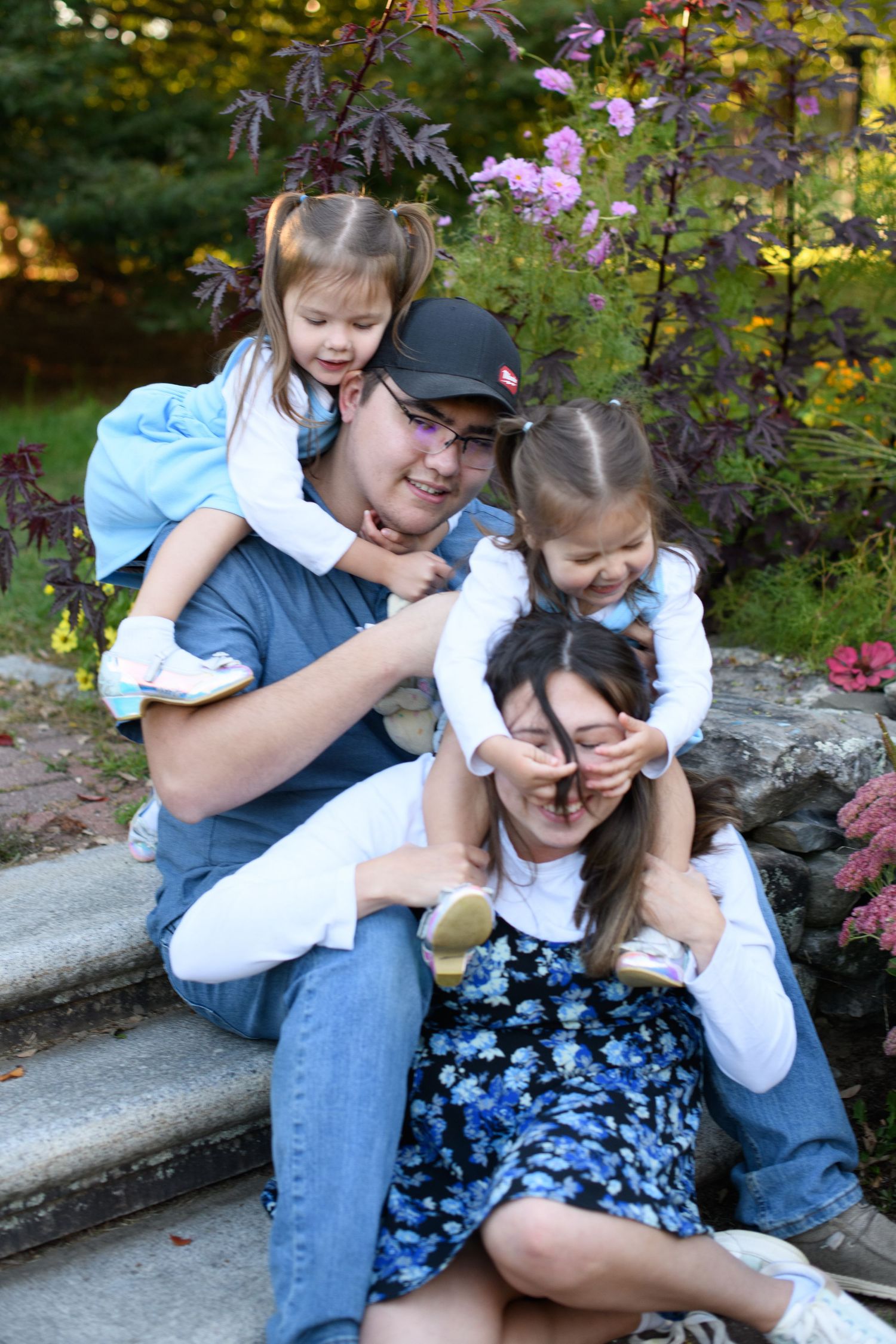 Playful family photo session in a garden with pink flowers and natural lighting.