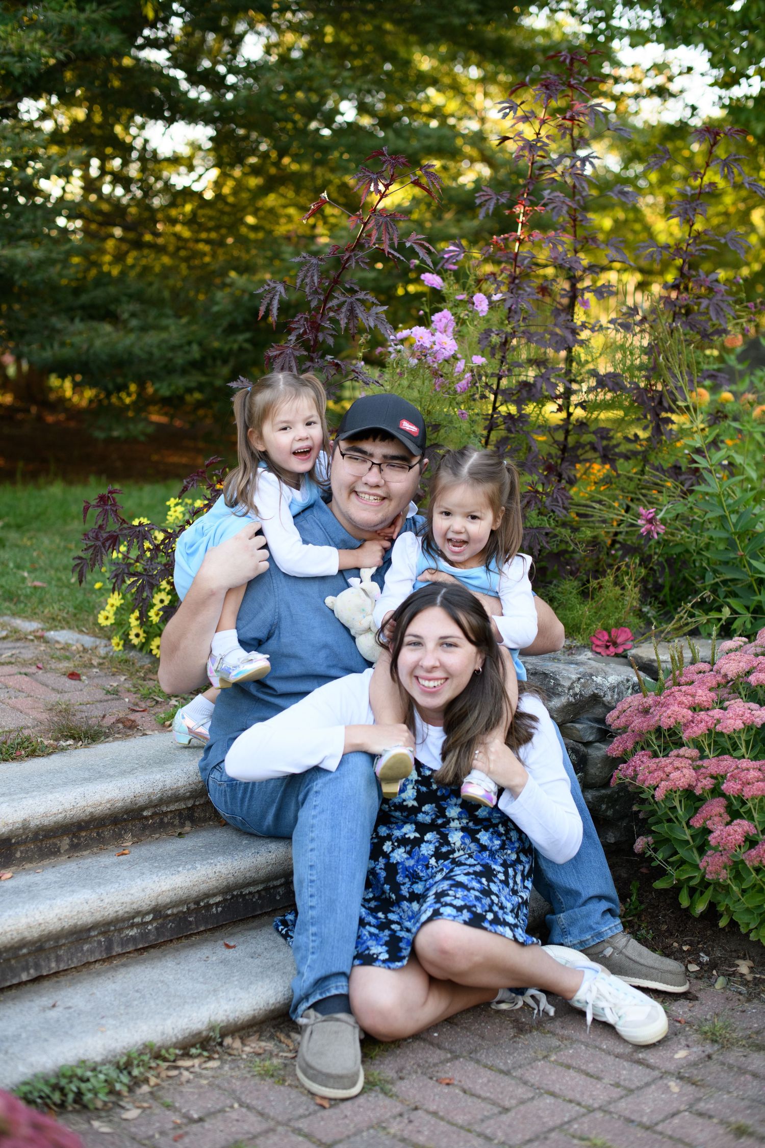 Family enjoying a casual photo session on stone steps surrounded by pink flowering bushes.