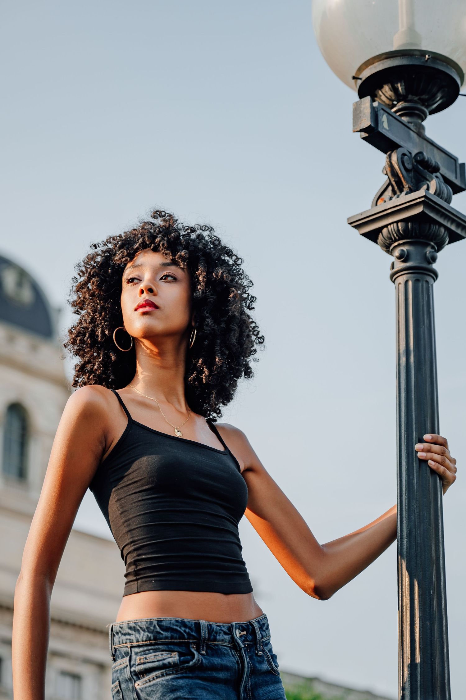 Fashion portrait against urban lampposts featuring casual street style and natural curls.