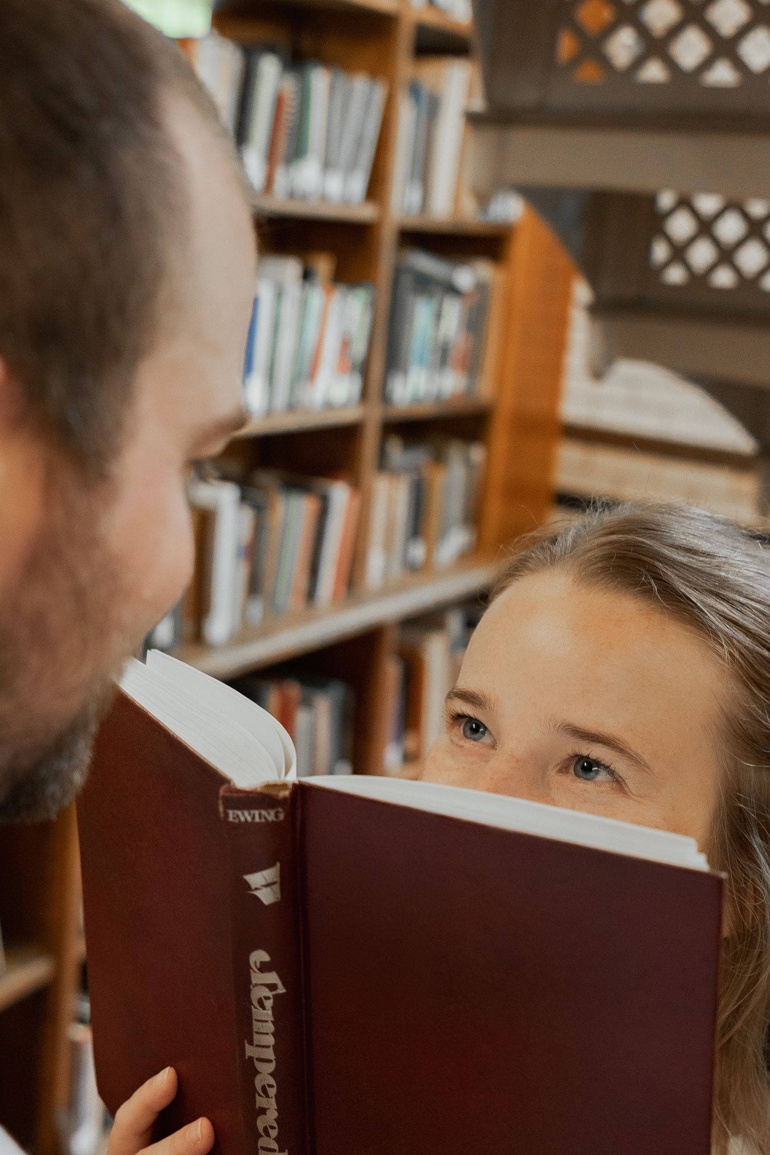 Playful couple peeking over a book during a romantic couples photography session at Linderman Library in Bethlehem PA
