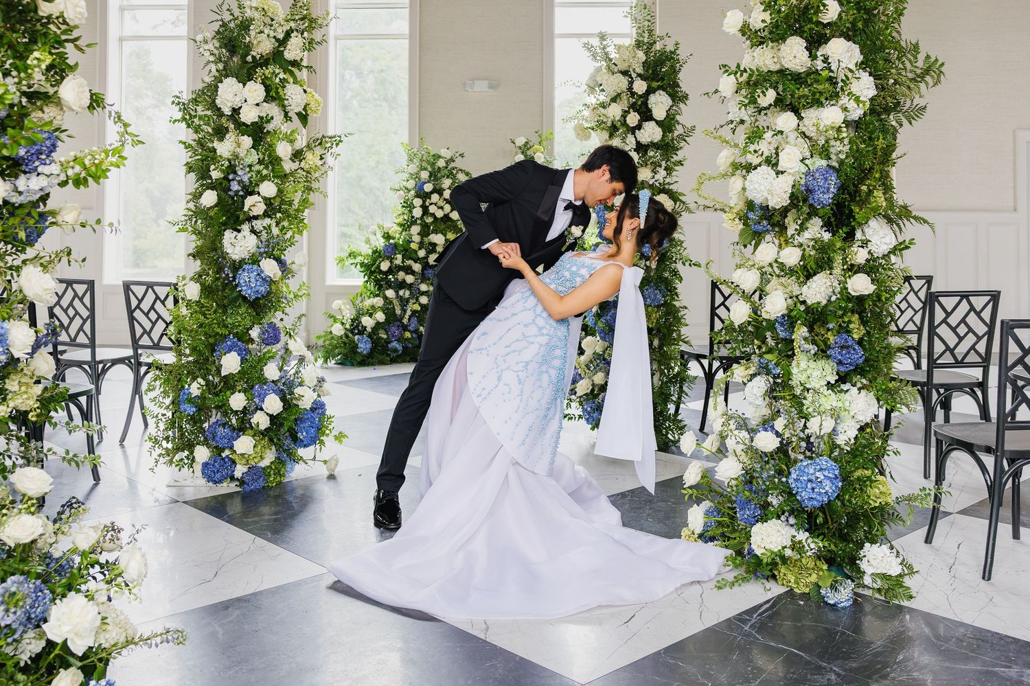 Bride and groom embracing beneath lush white and blue florals during an editorial wedding at Elkins Estate in Elkins Park, Pennsylvania.