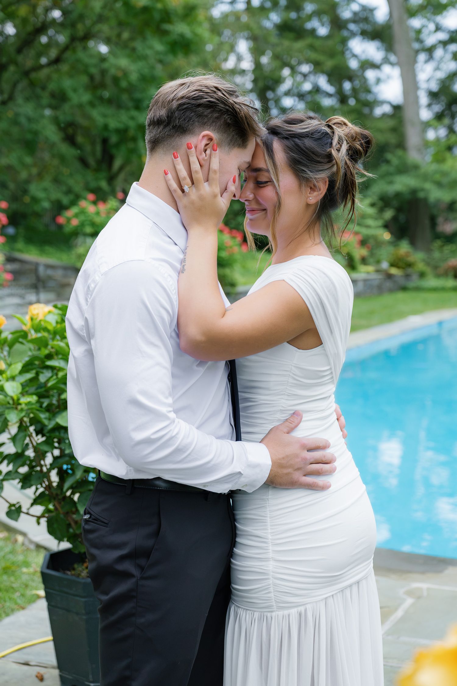 Engaged couple embracing beside the pool at Conestoga House and Gardens during their engagement session in Lancaster, Pennsylvania.