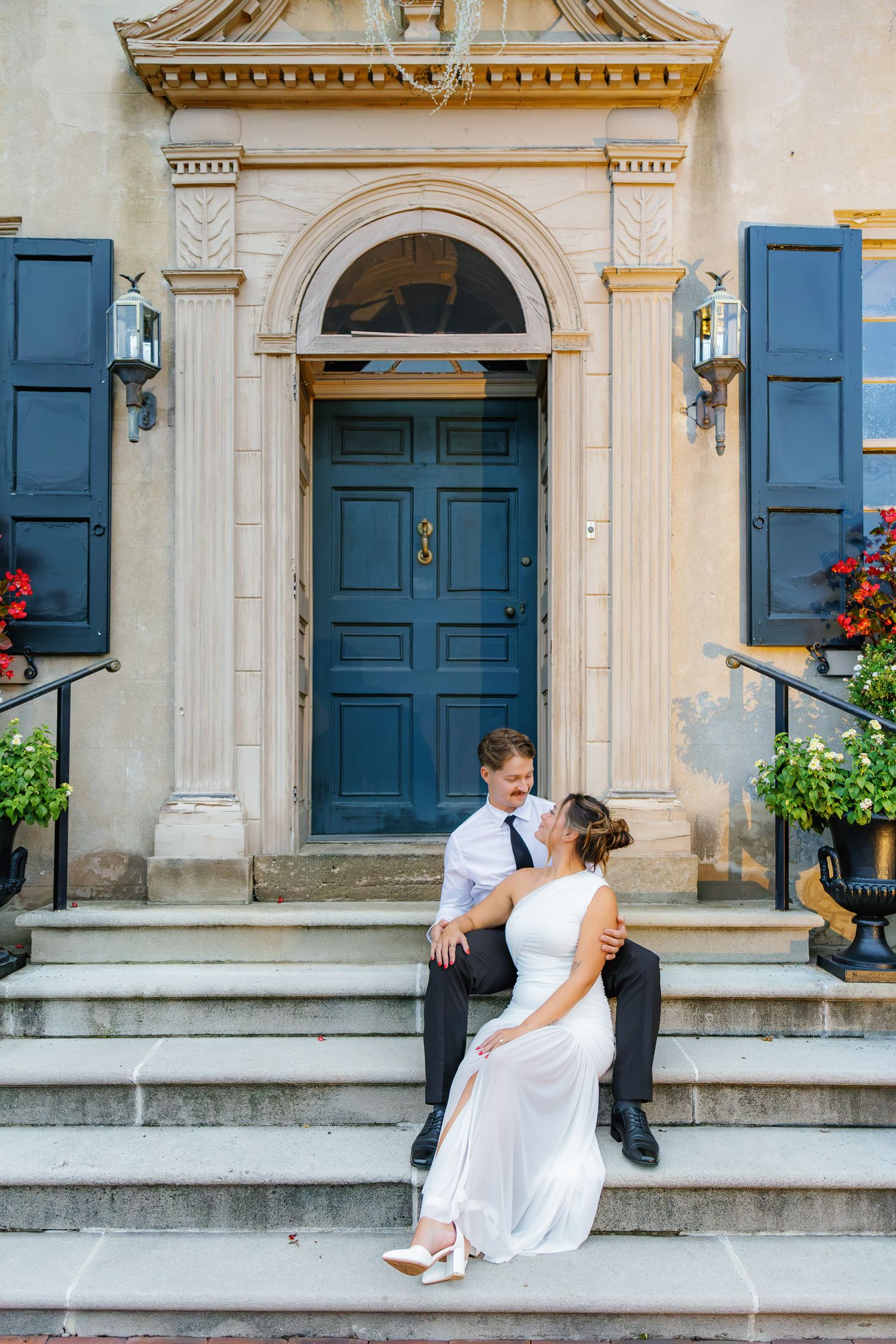 Engaged couple sitting together on the steps outside the distinctive blue and gold entrance at Conestoga House and Gardens in Lancaster, PA