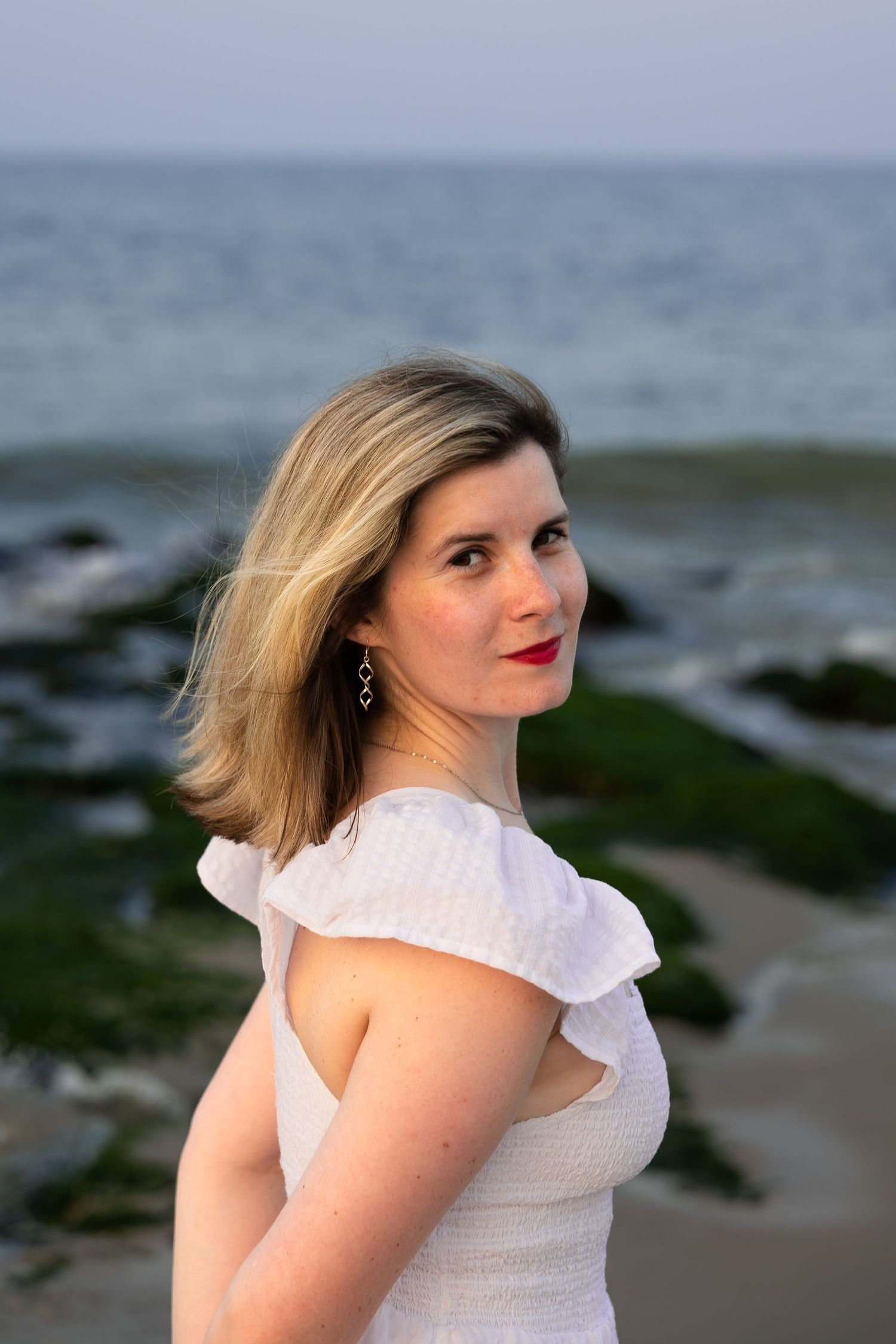 Woman looking toward the camera by the ocean during a natural light beach portrait photography session