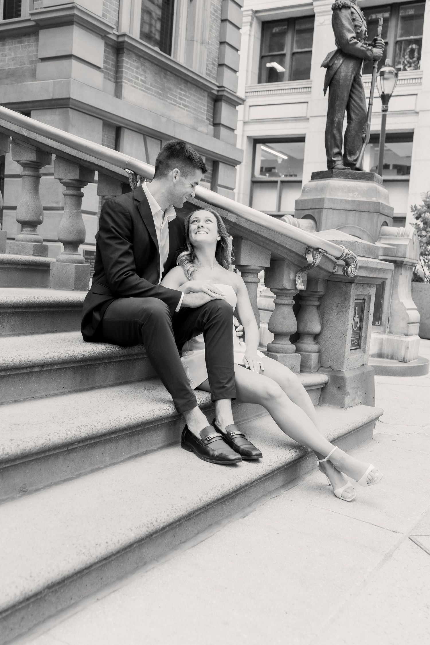 Black-and-white engagement portrait of a couple sitting together on the steps of Philadelphia City Hall.