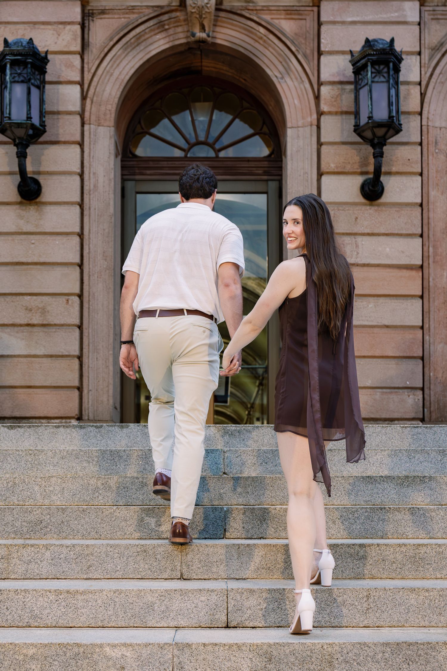 Couple walking hand in hand up the steps of a historic building during their downtown Lancaster, Pennsylvania engagement session.
