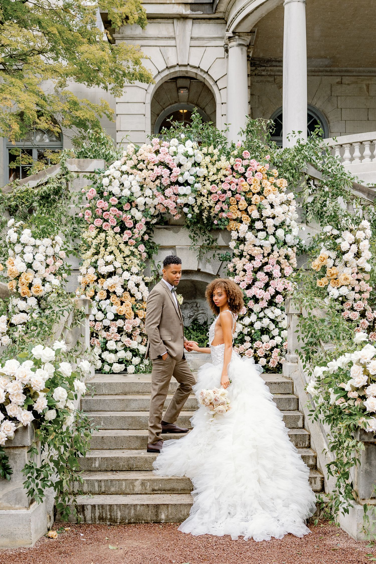 Bride on the floral-covered staircase at Elkins Estate, an elegant historic wedding venue near Philadelphia, Pennsylvania.