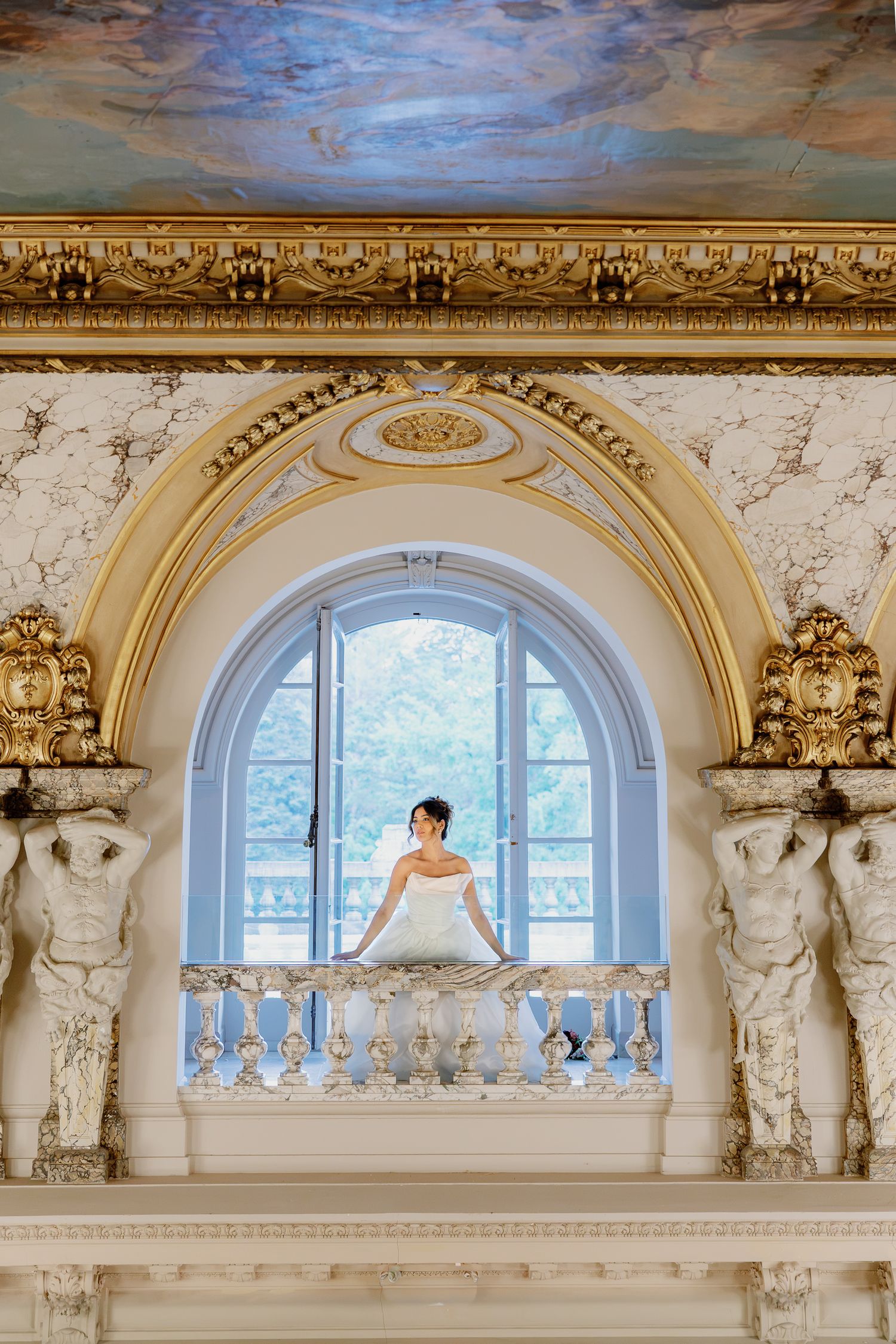 Editorial bridal portrait framed by the ornate architecture and arched window inside Elkins Estate near Philadelphia.
