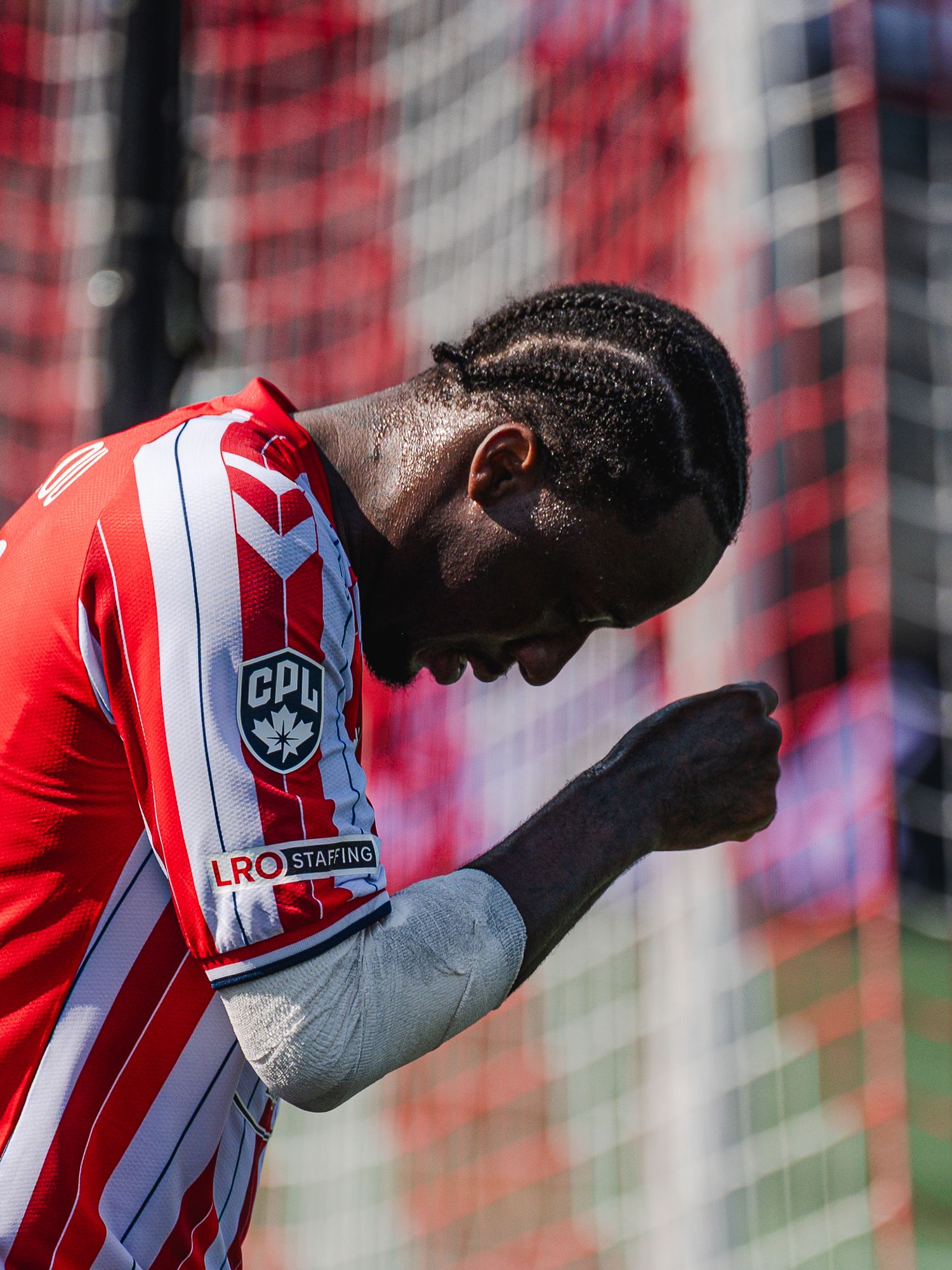 Soccer player in red CPL jersey celebrates with fist pump in front of goal net.
