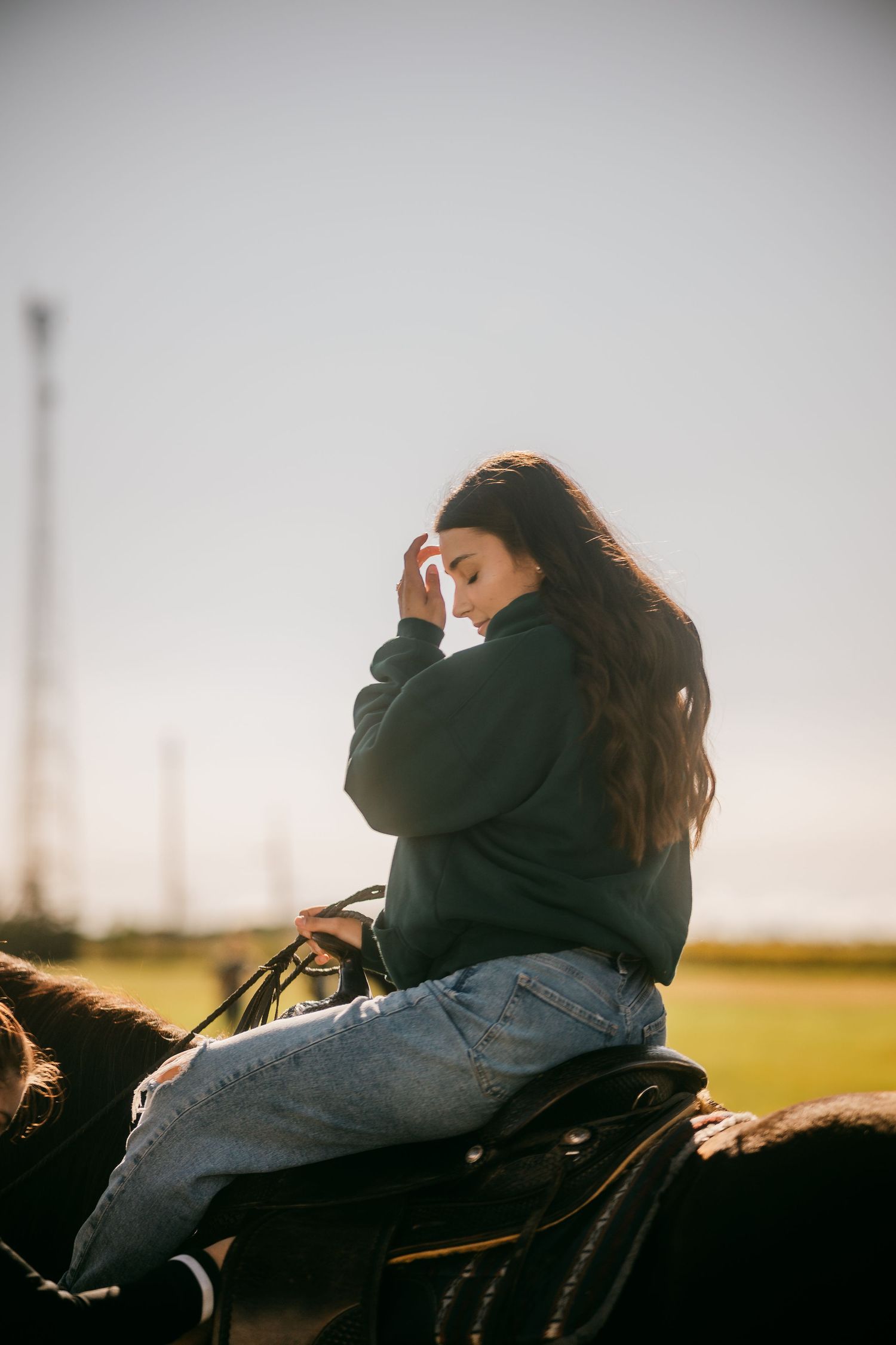 Young woman with long dark hair riding a horse at sunset in an open field.