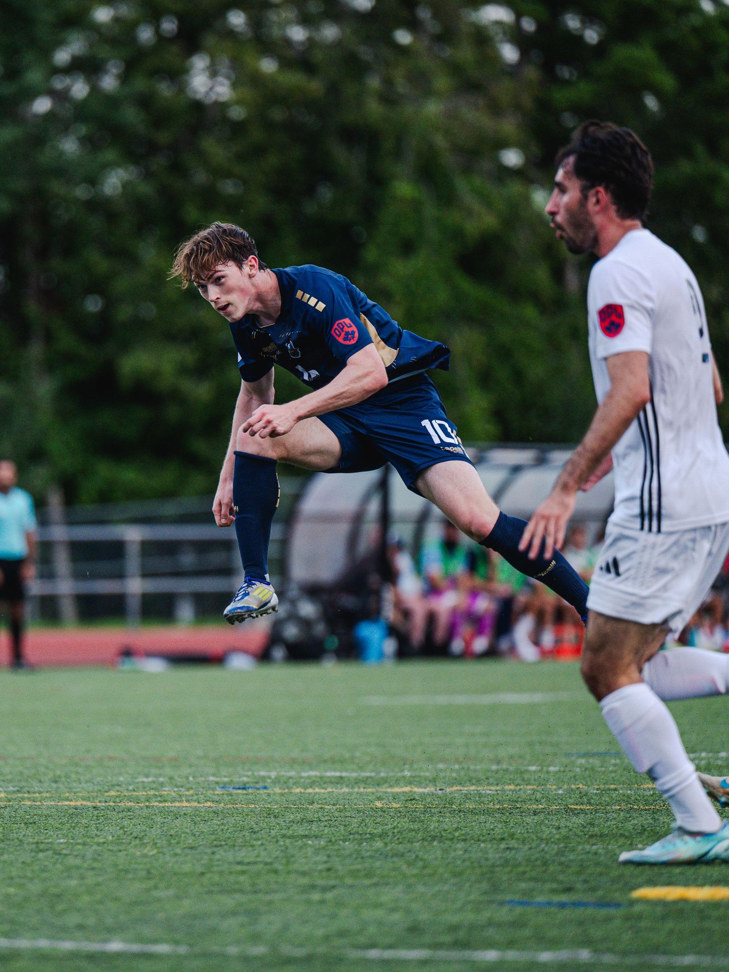 Soccer player wearing number 10 jersey leaps dynamically during a competitive match on a green turf field.