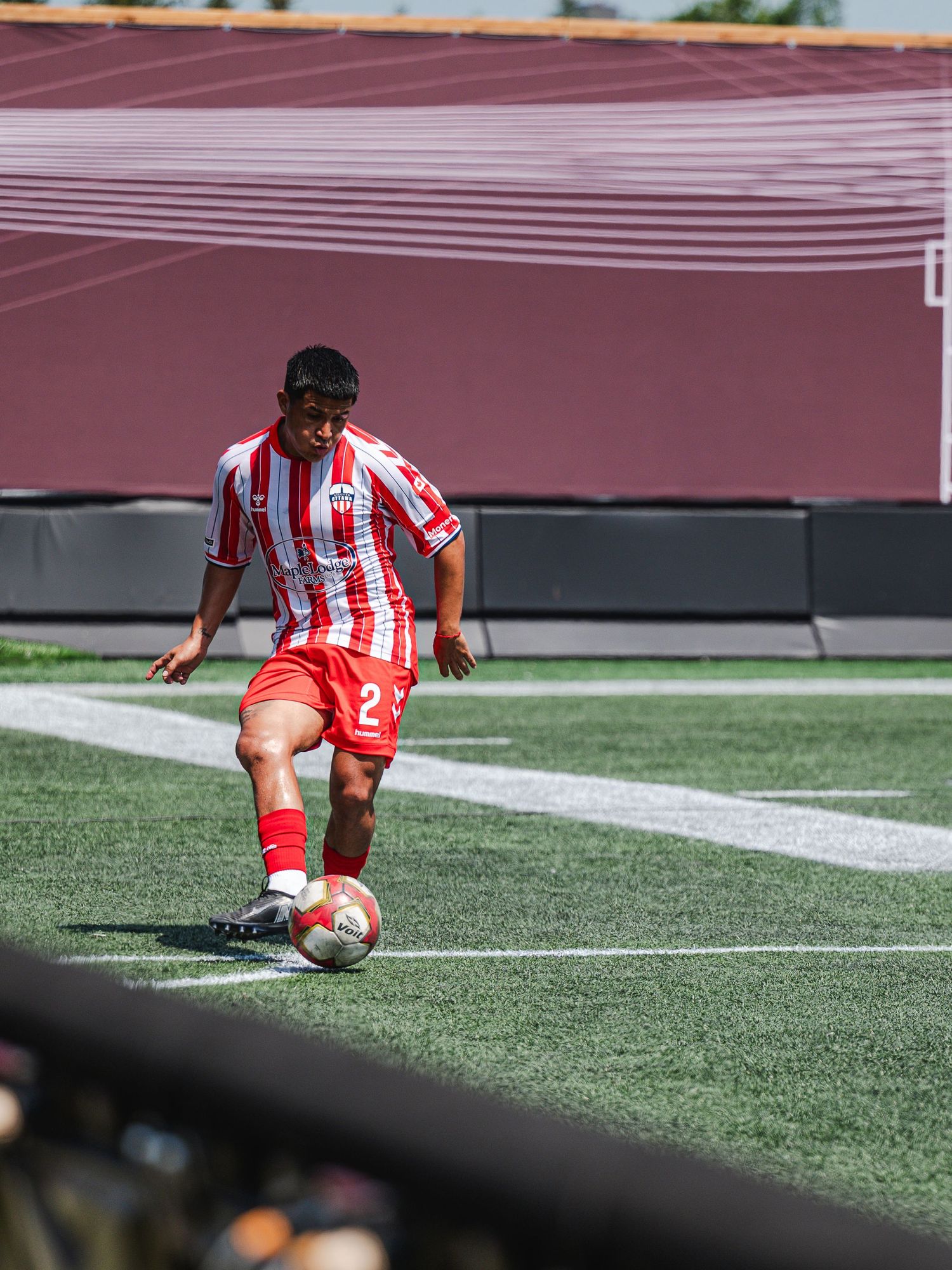 Soccer player in red and white striped jersey number 2 controls ball during sunny match.