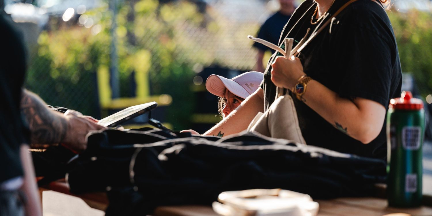 Person sitting at an outdoor table writing in a notebook with sports equipment and a water bottle nearby.