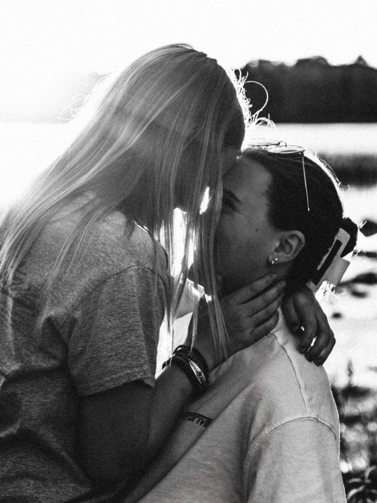 Romantic black and white photo of a couple sharing a tender kiss outdoors near a lake.