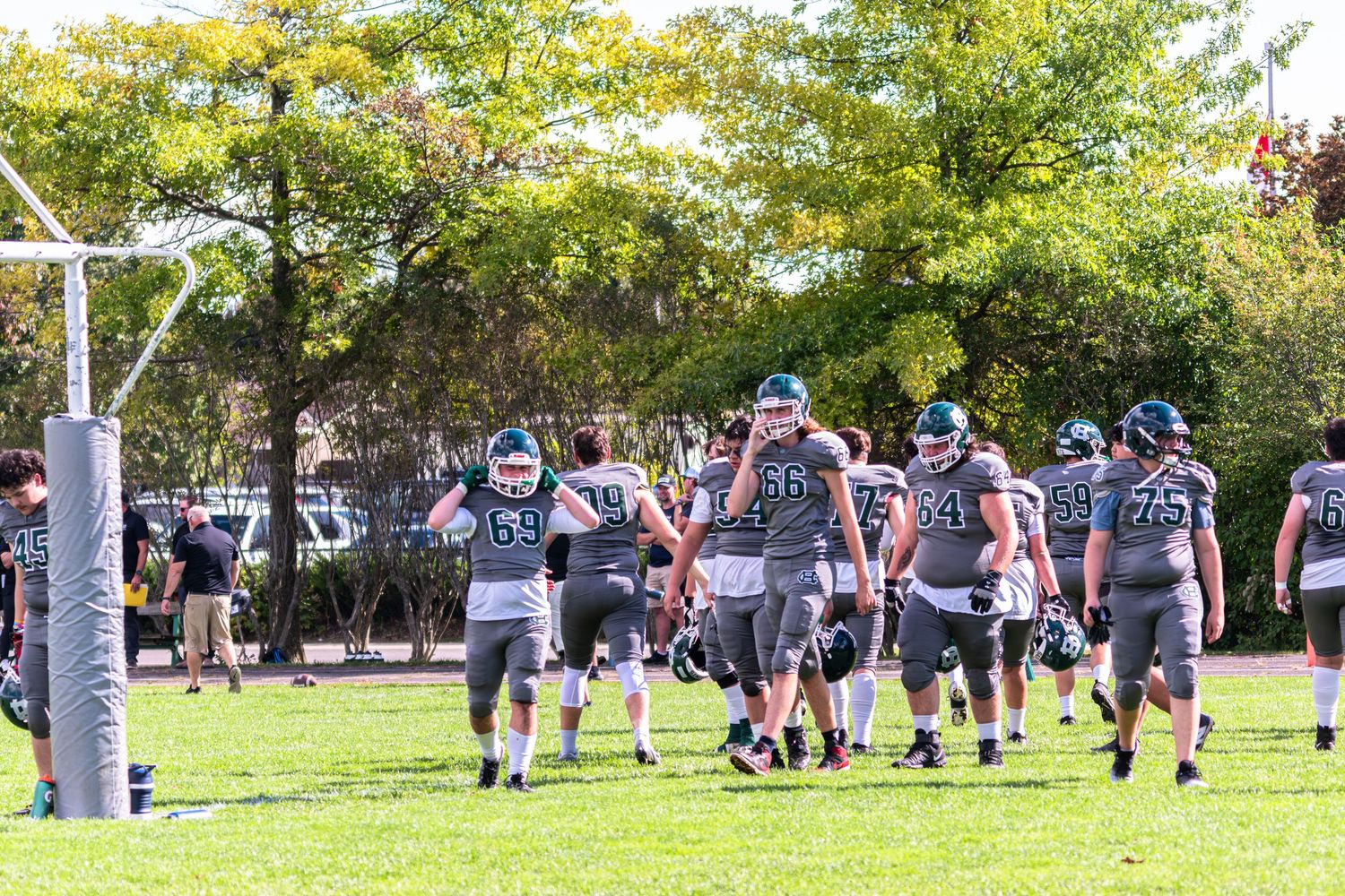 Football players in green uniforms walking across a field during an outdoor practice session.