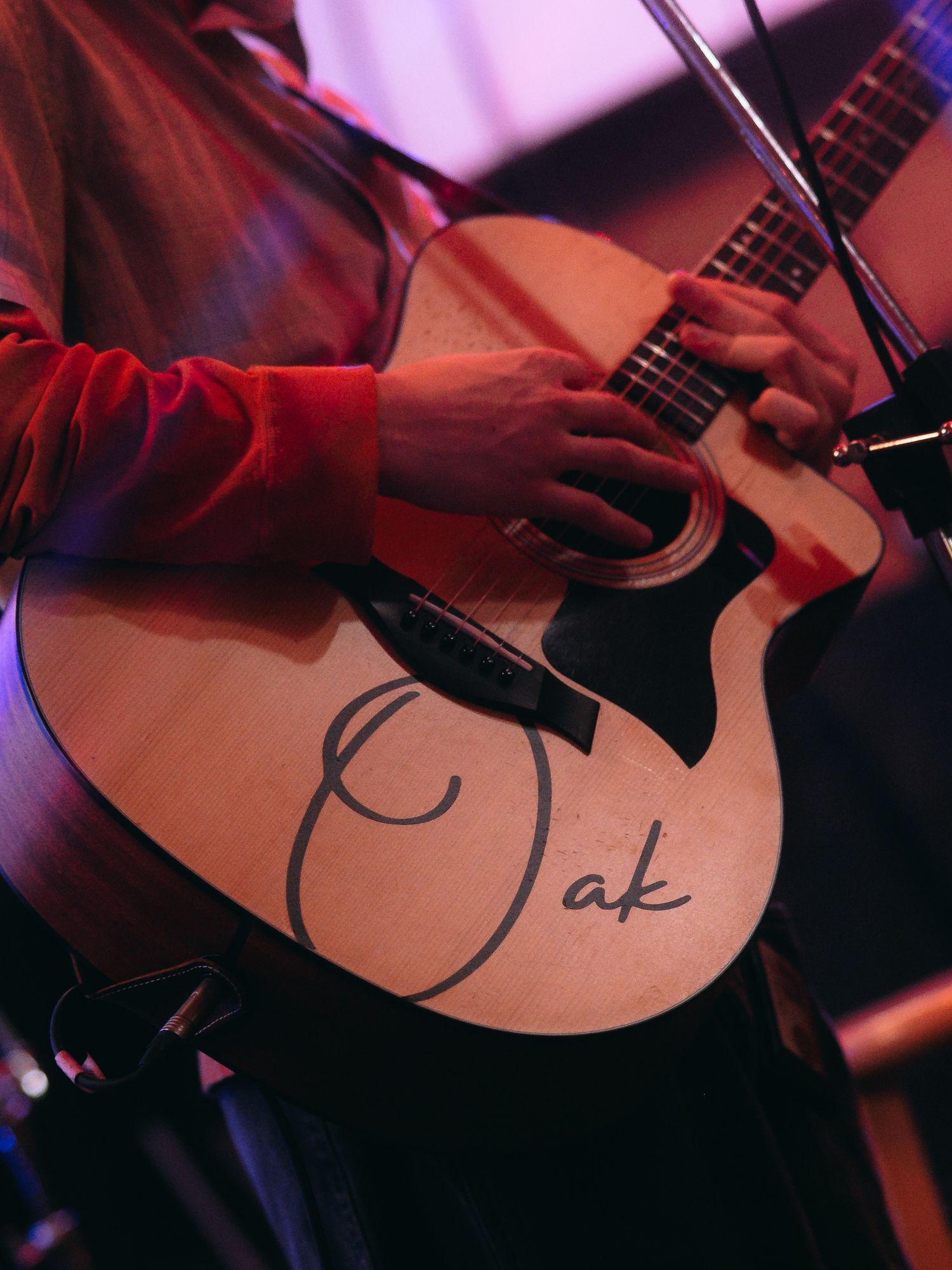 Close-up of hands playing an acoustic guitar with Oak written on the body during a live performance.