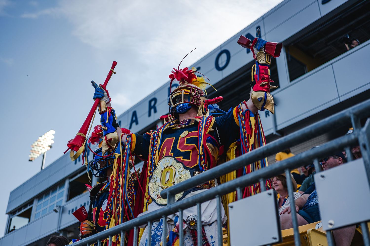 Colorfully costumed Queen's football fan cheers enthusiastically in stadium stands during game.