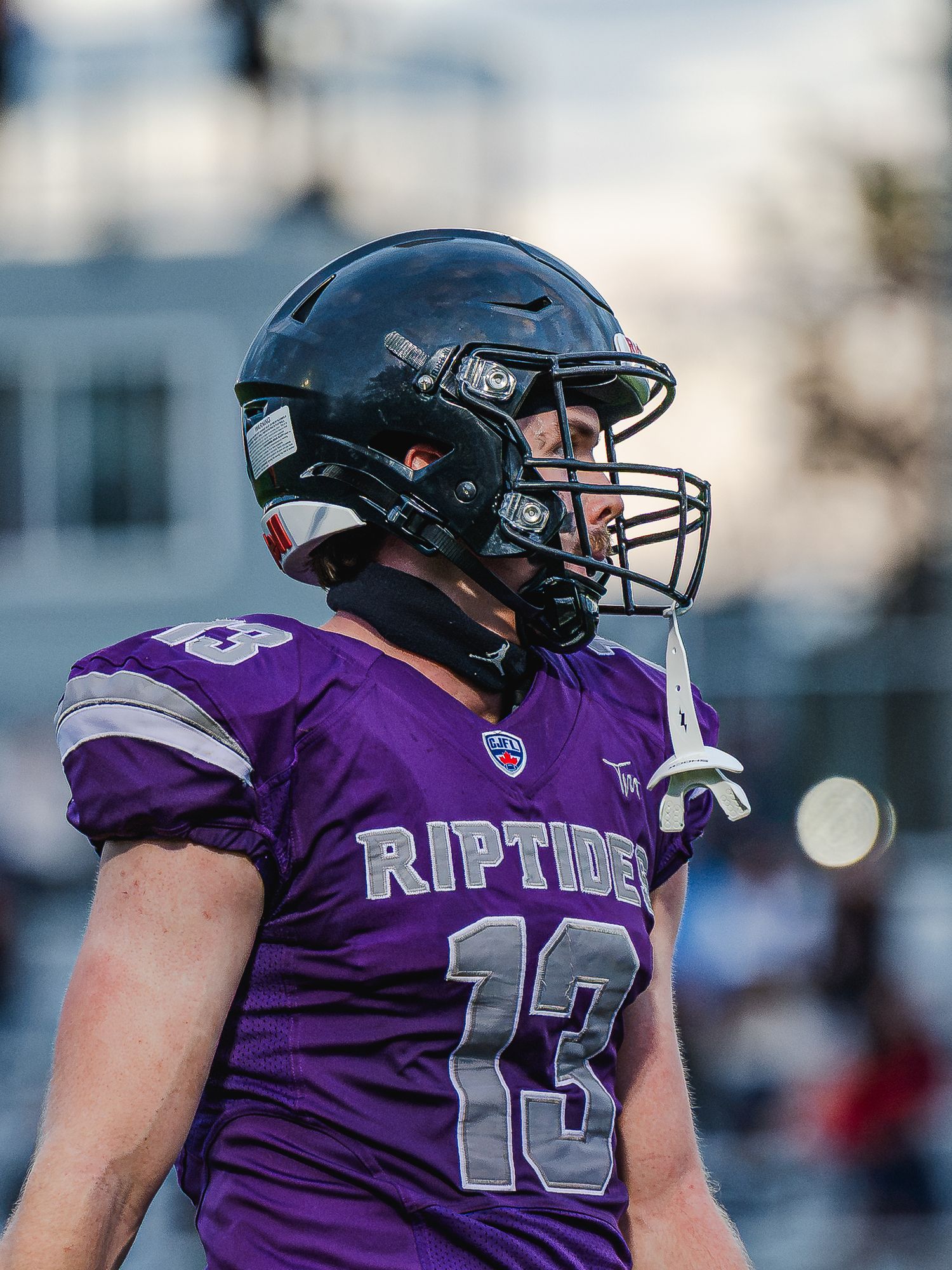 Riptides football player wearing purple jersey number 13 and black helmet on field at dusk.