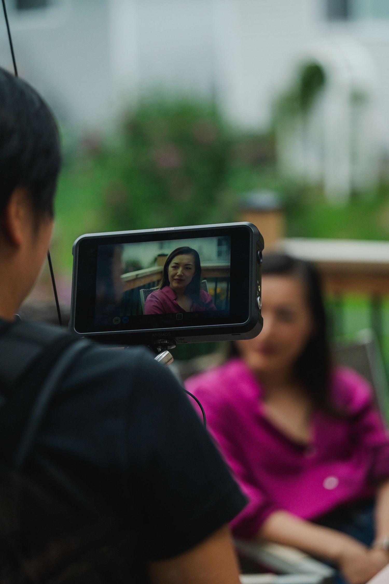 A camera monitor displays a woman in pink being filmed during an outdoor interview session.