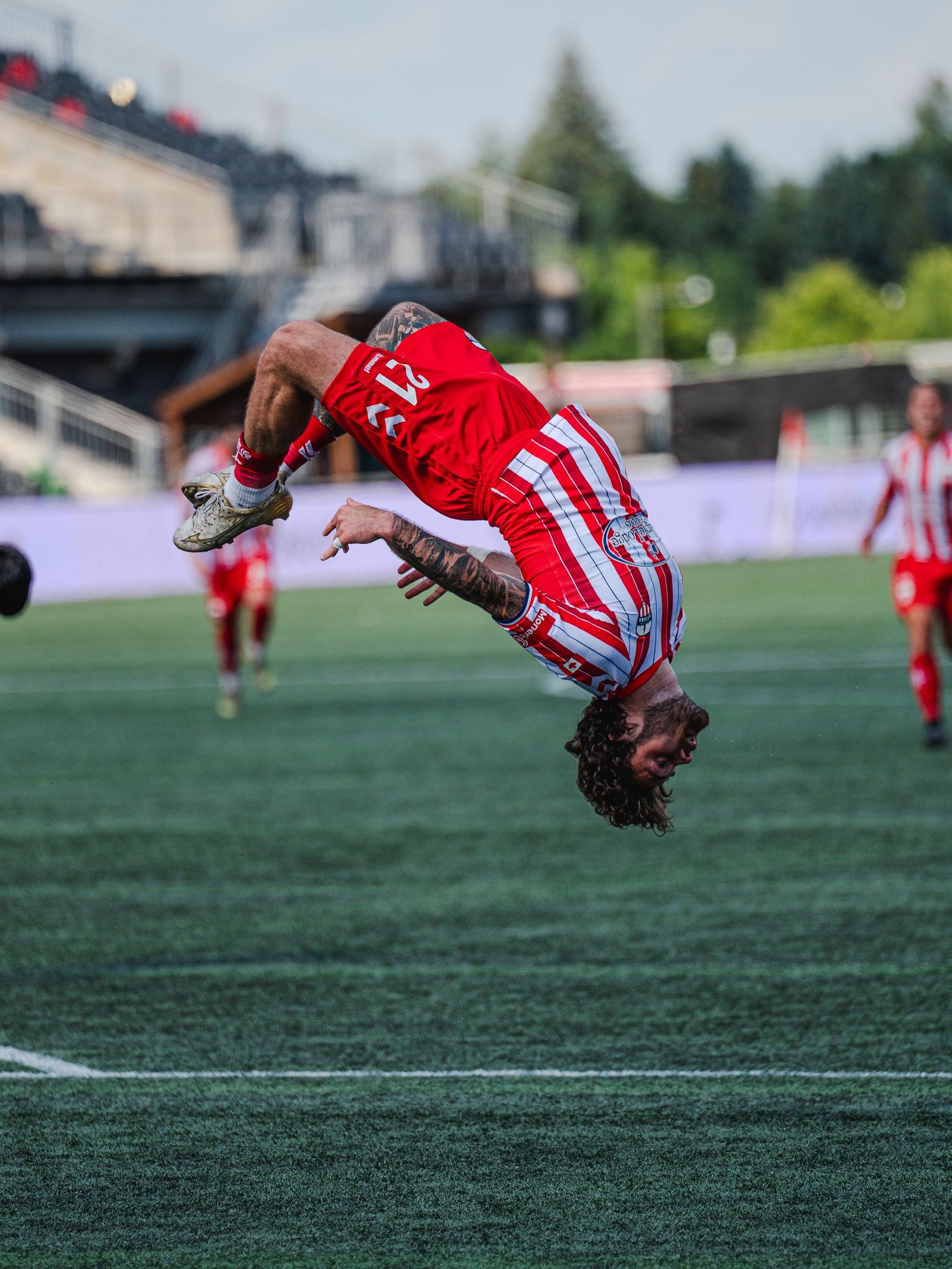 Soccer player performing backflip celebration on green field during match.