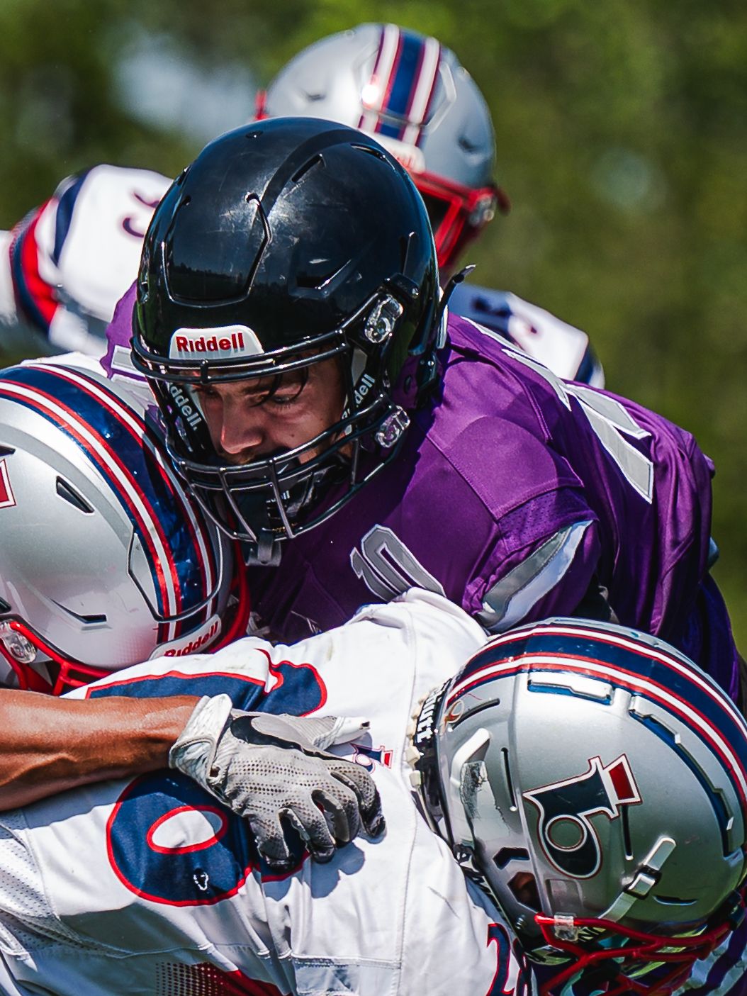 Purple-jersied Riptides player tackles opponent in red and white uniform during football game.