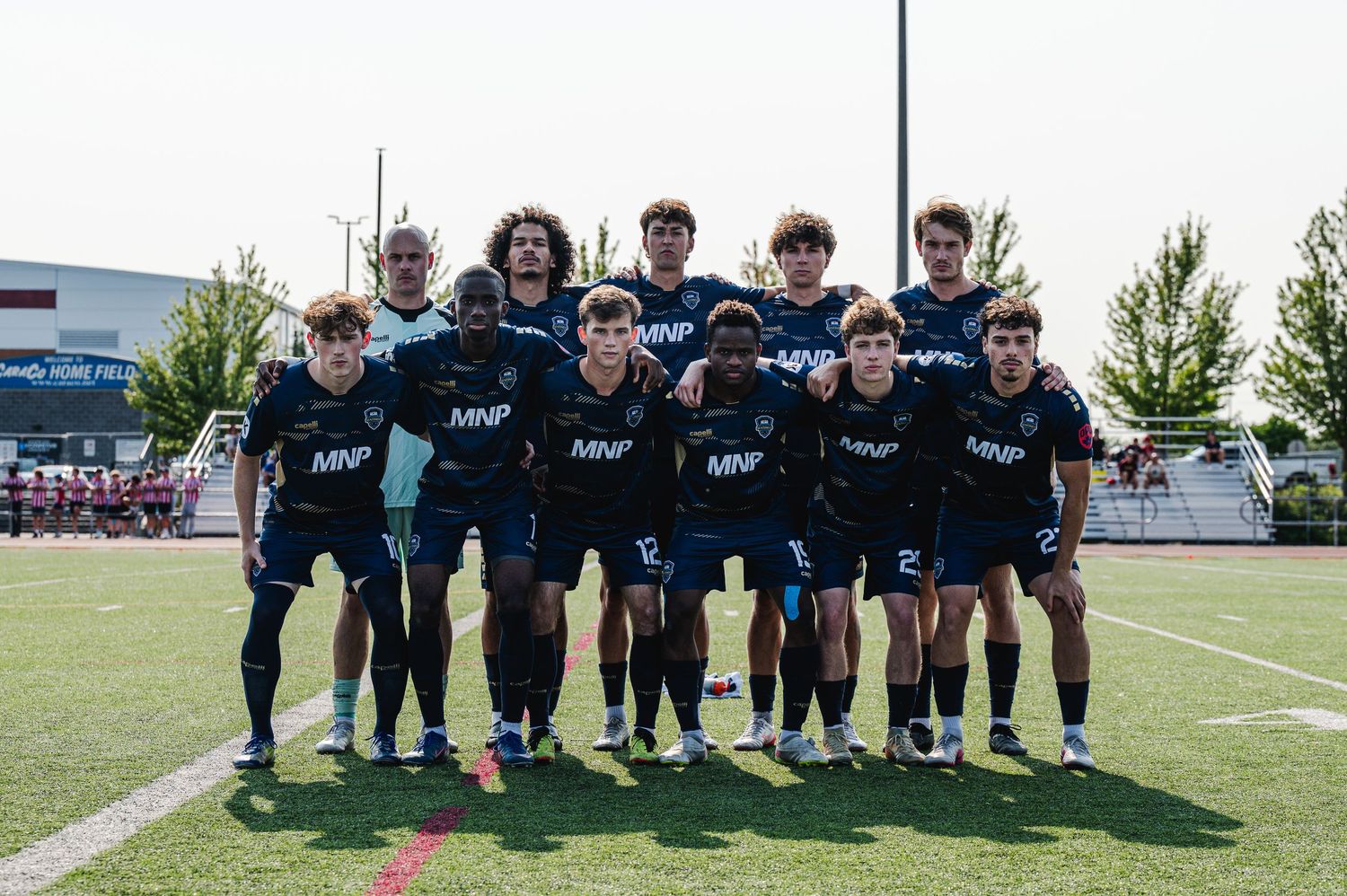 Youth soccer team poses for a group photo on a sunny field before a competitive match.