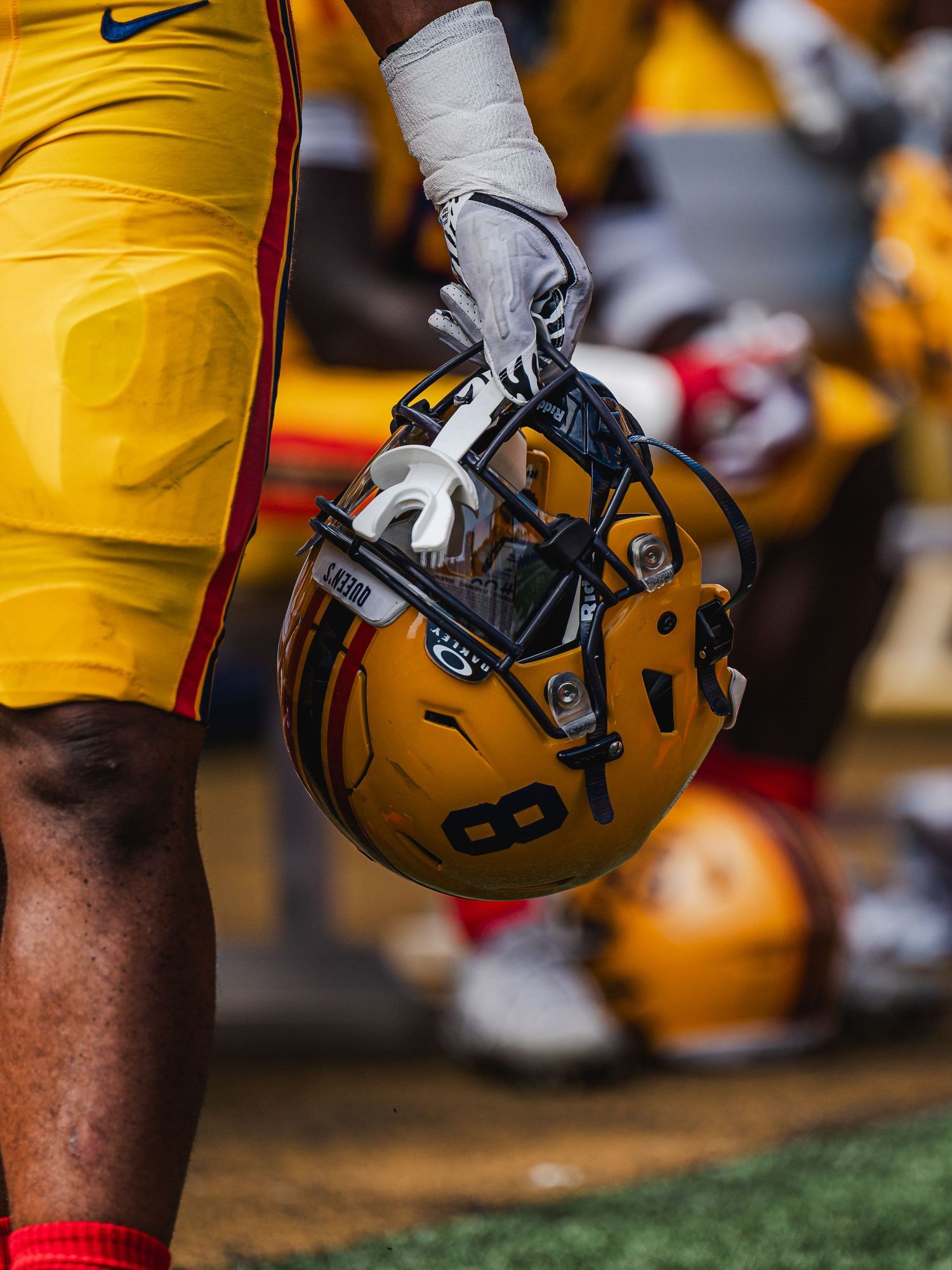 Football player holds gold helmet with number 8 on sideline.