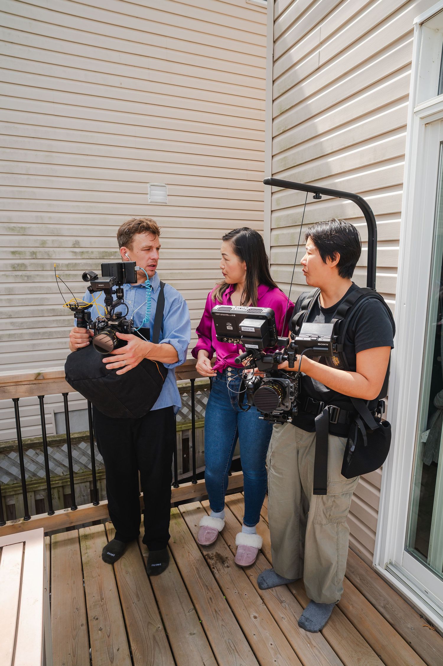 Three film crew members discussing production on outdoor deck with professional camera equipment.