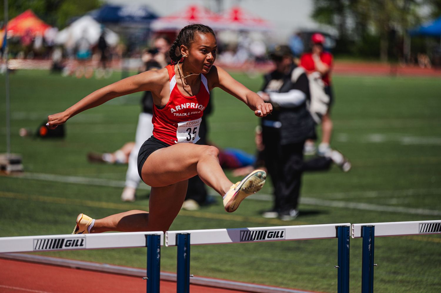 Female athlete in red uniform clearing a hurdle during an outdoor track and field competition.