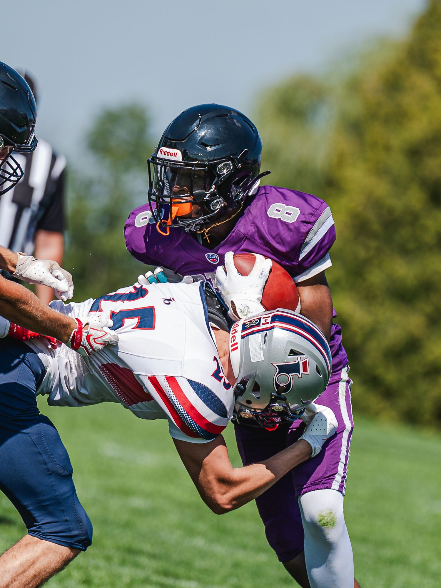 Number 89 purple jersey receiver catches the ball while being tackled by a white-uniformed defender.