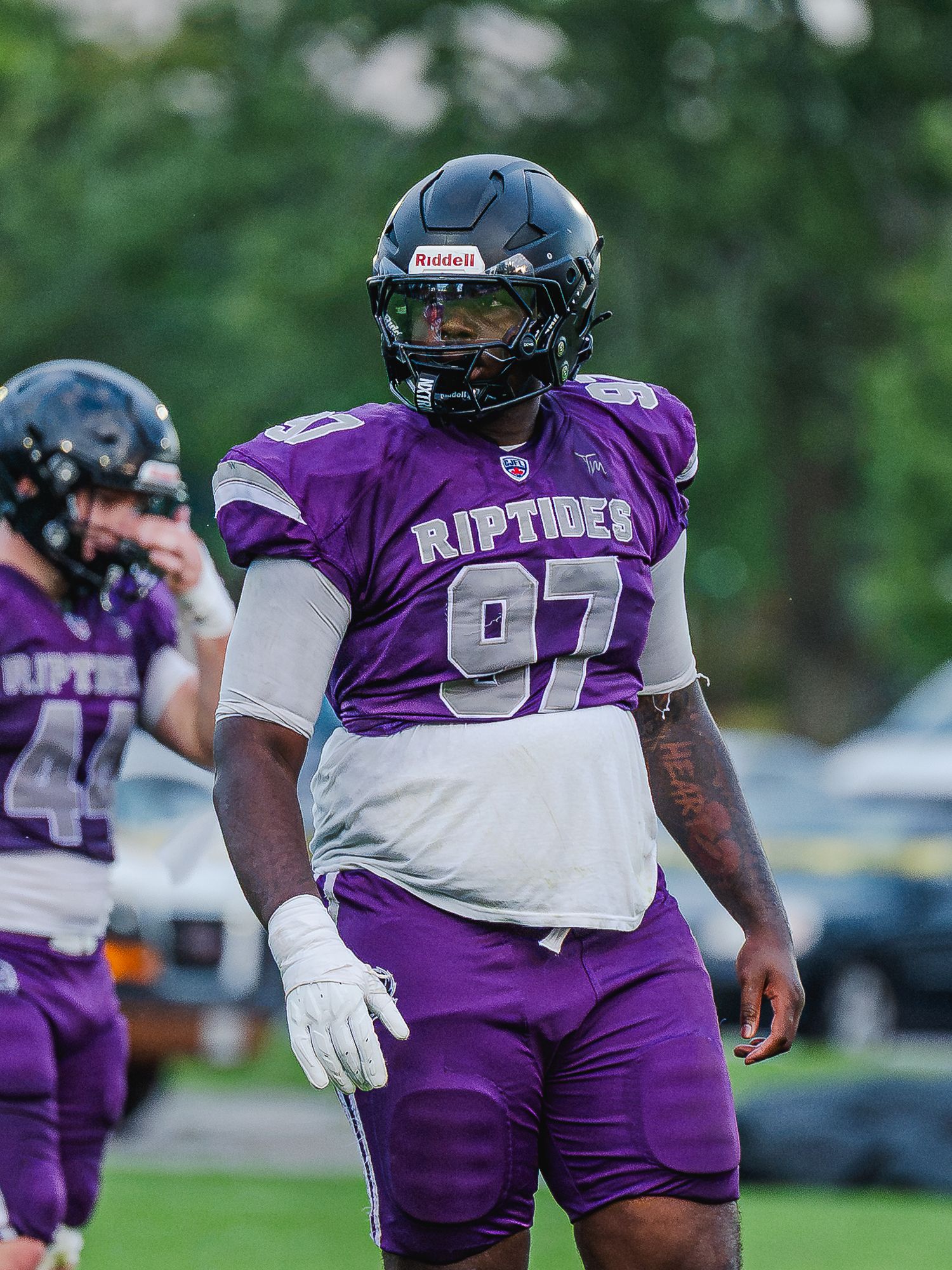 Riptides football player number 97 in purple uniform stands on field during practice or game.
