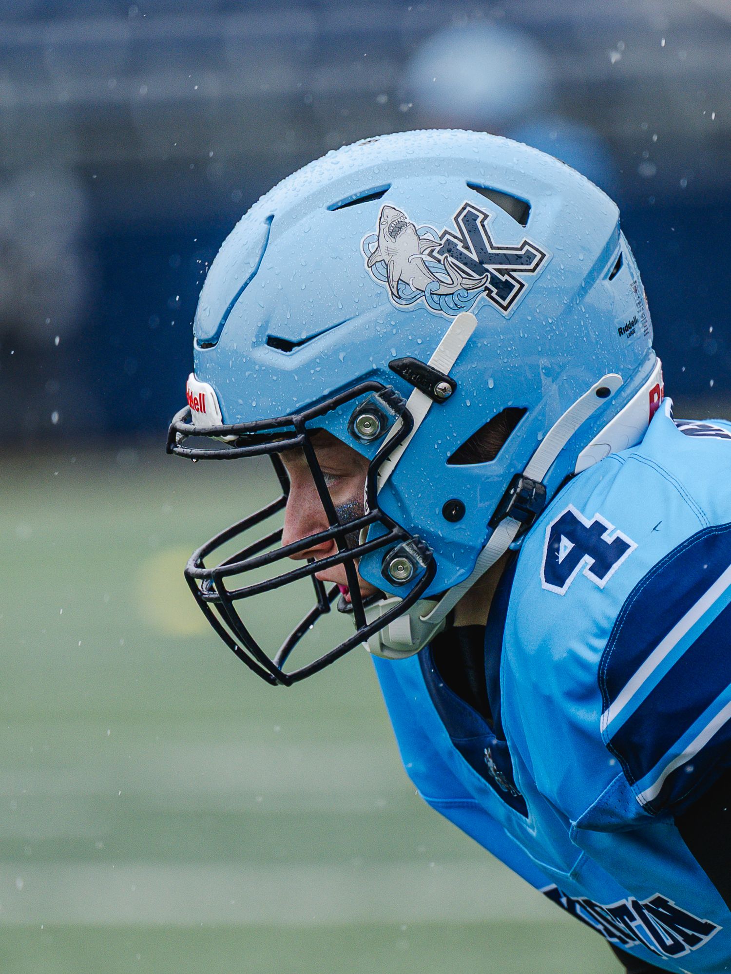 Close-up of a football player wearing a light blue helmet with a wolf logo in rainy game conditions.