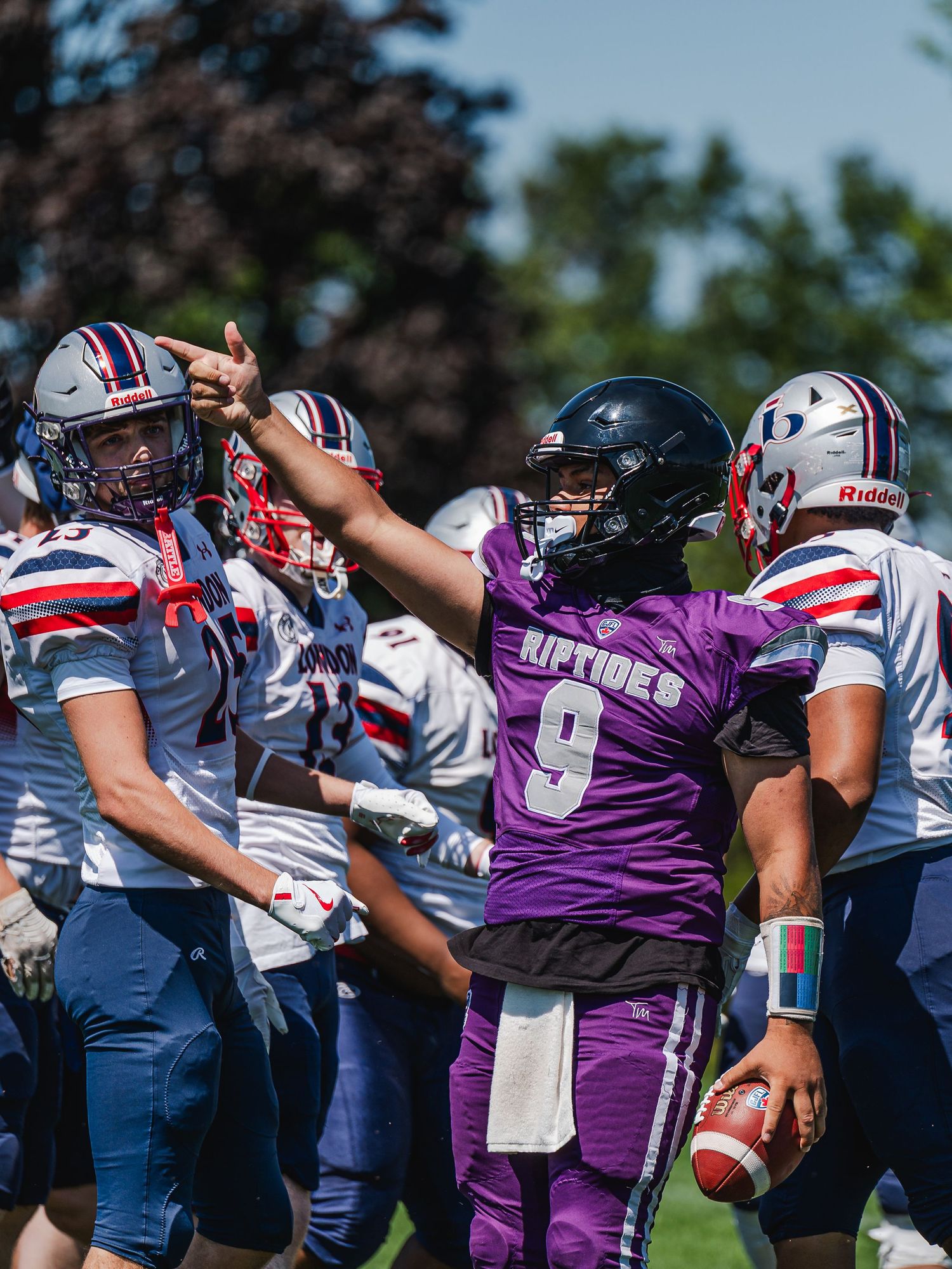 Riptides quarterback #9 in purple jersey signals first down during outdoor football game.