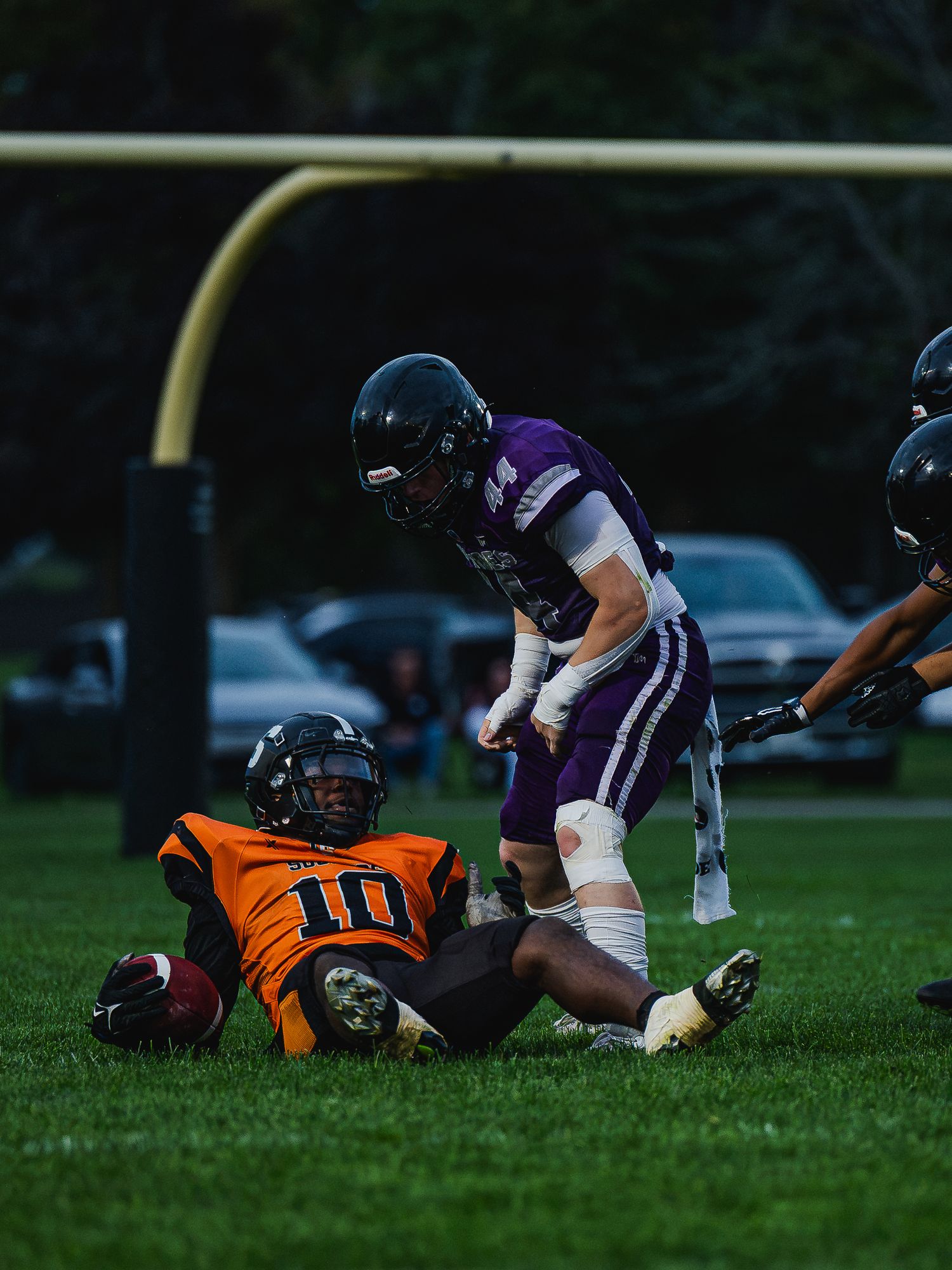 Riptides football player stands over fallen opponent wearing orange jersey number 10 on field.