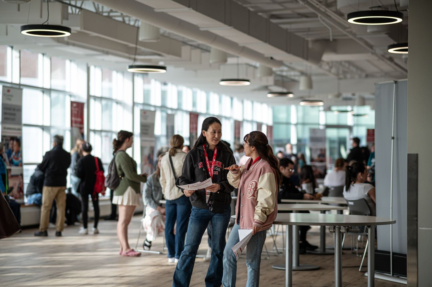 Students networking and conversing in a modern open-concept university building with large windows.