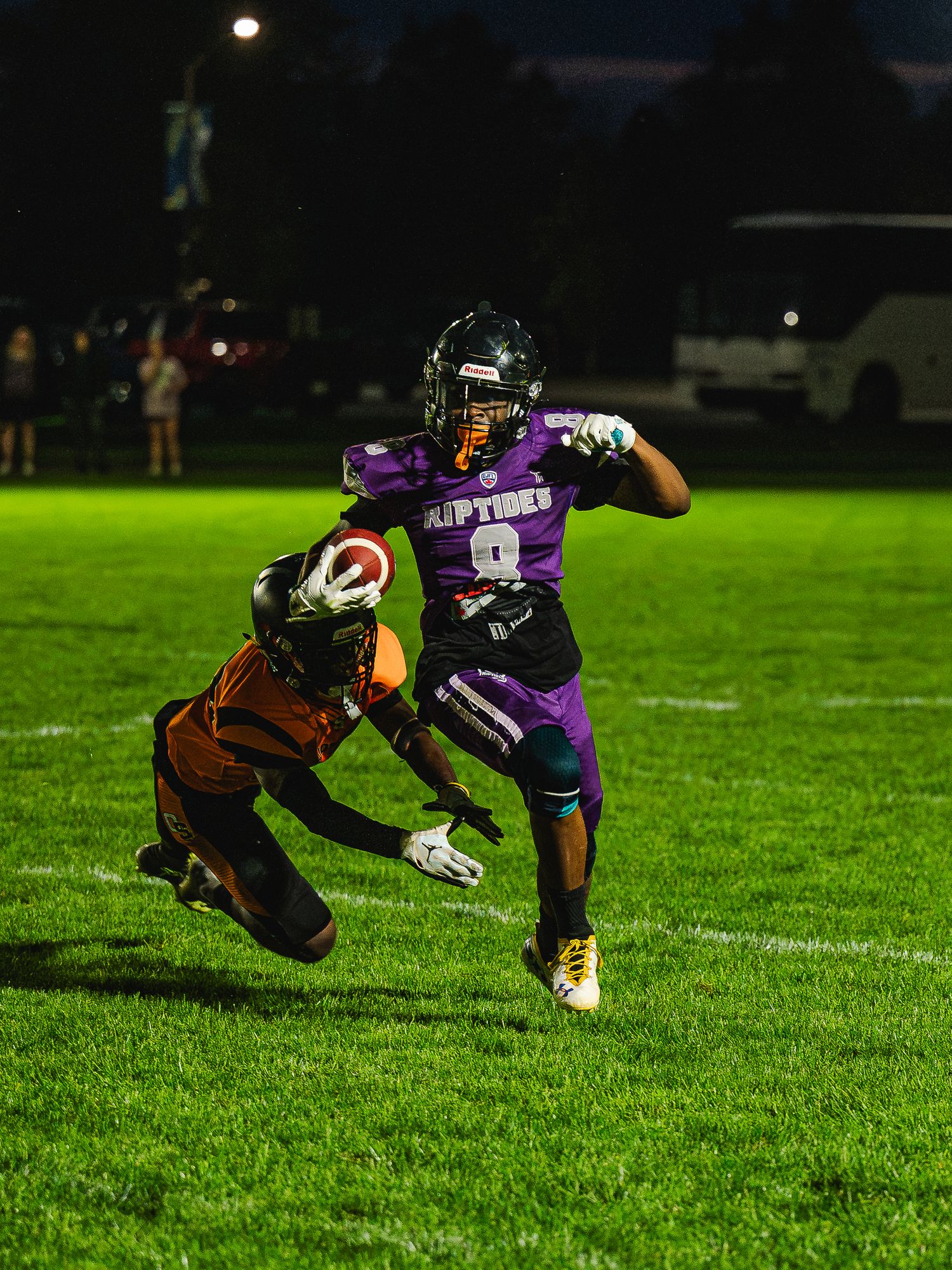 Purple Riptides football player evades tackle during night game.