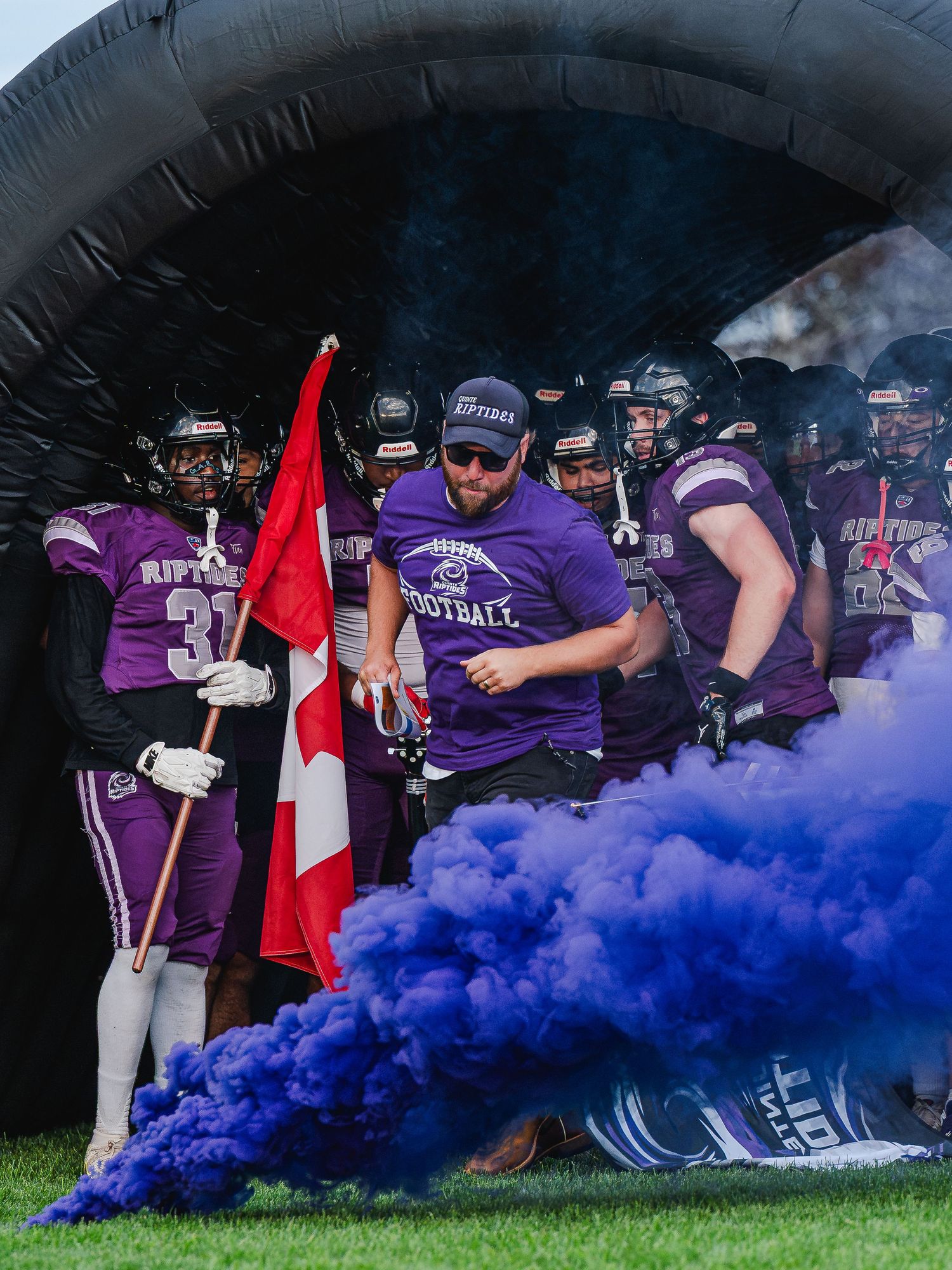 Riptides football team emerges through tunnel with purple smoke and Canadian flag before game.