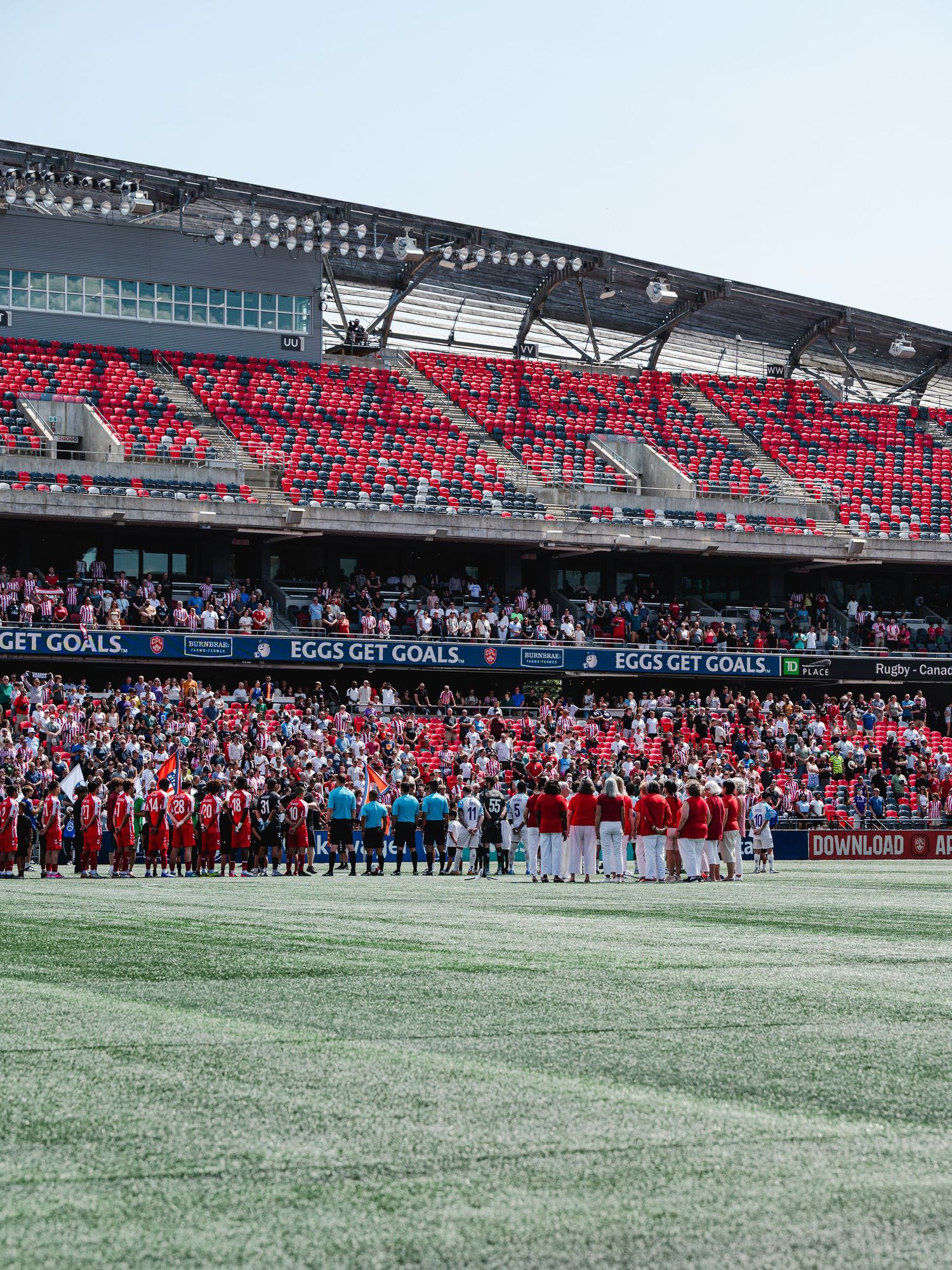 Soccer teams line up on field before match in a large stadium with red seats and crowd.