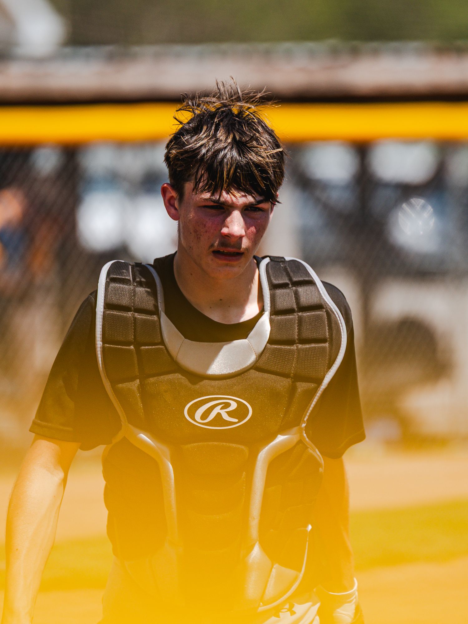 Young baseball catcher wearing Rawlings chest protector gear on sunny field.