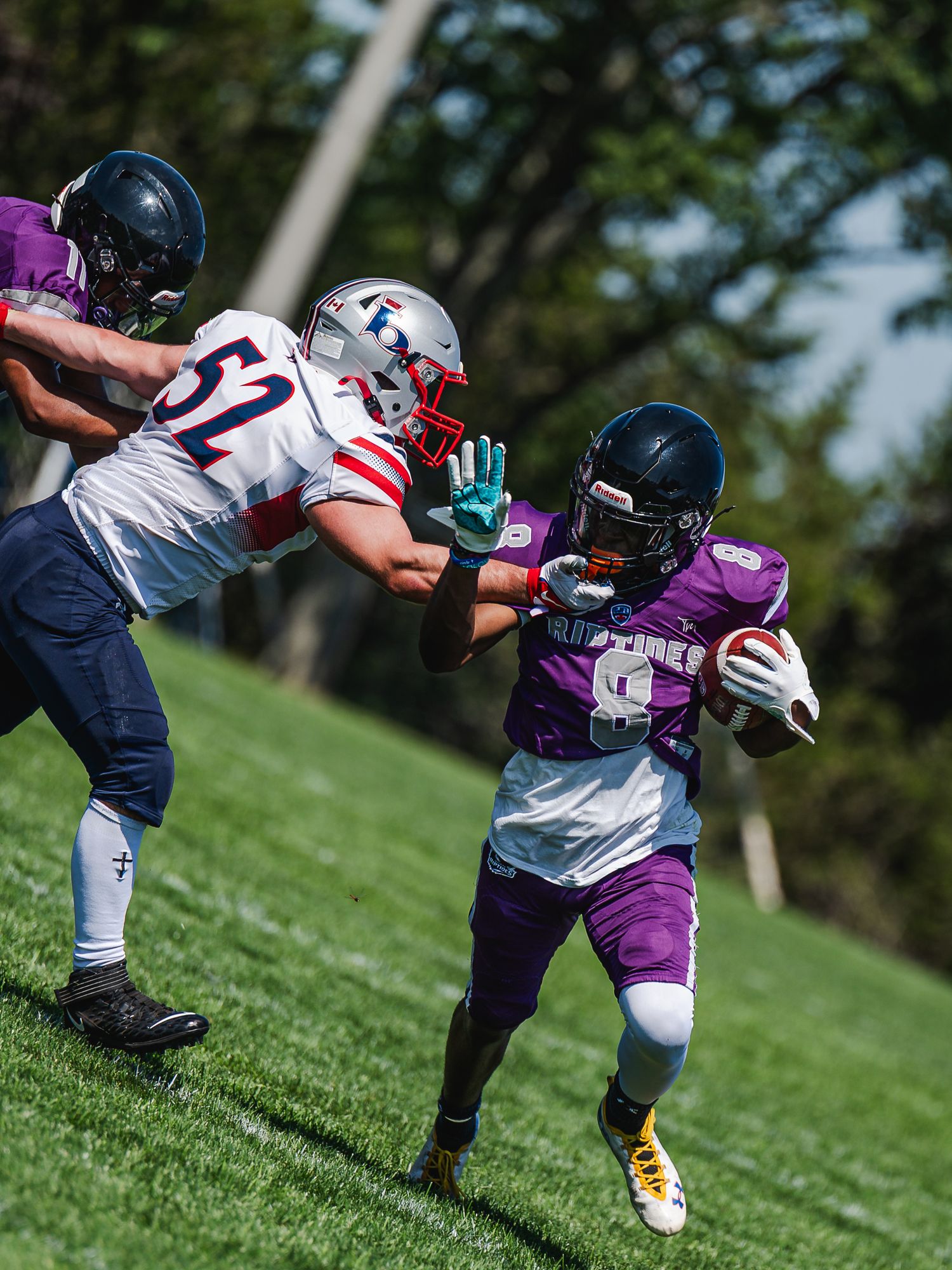 Purple jersey football player carries the ball while evading a tackle from a white-uniformed defender.