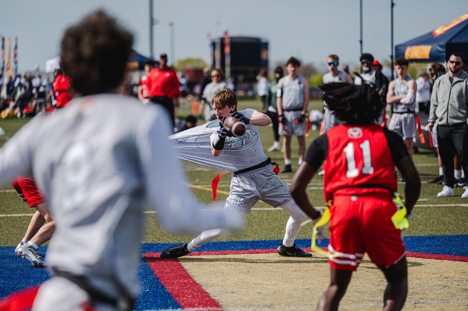 Flag football quarterback throwing a pass during an outdoor tournament on a sunny day.