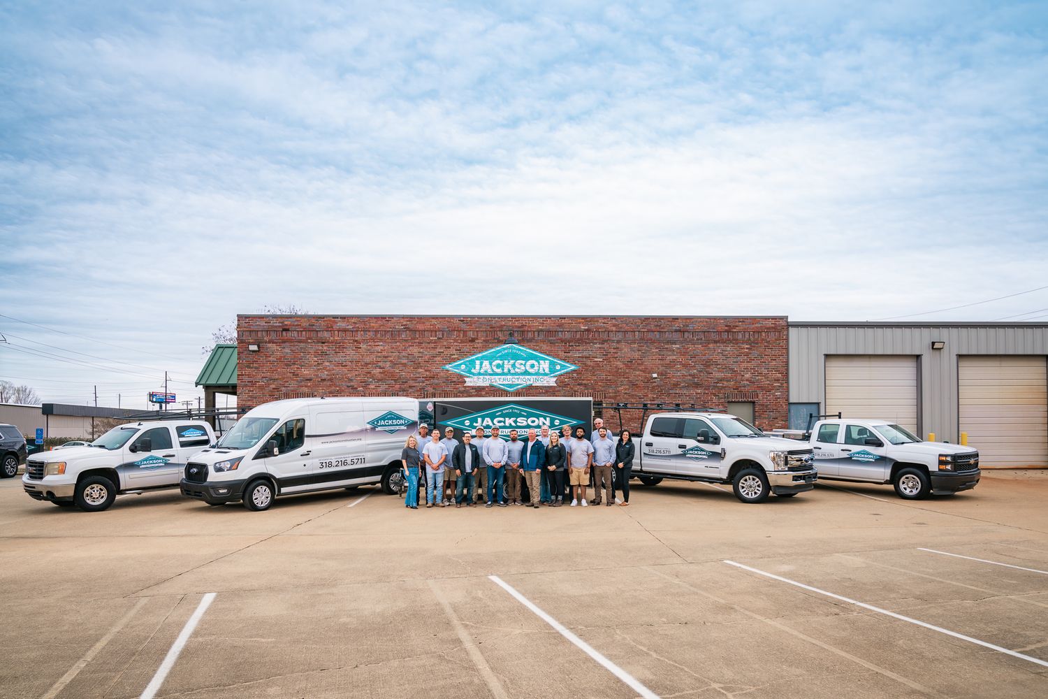Jackson service team poses with branded fleet vehicles outside brick office building.