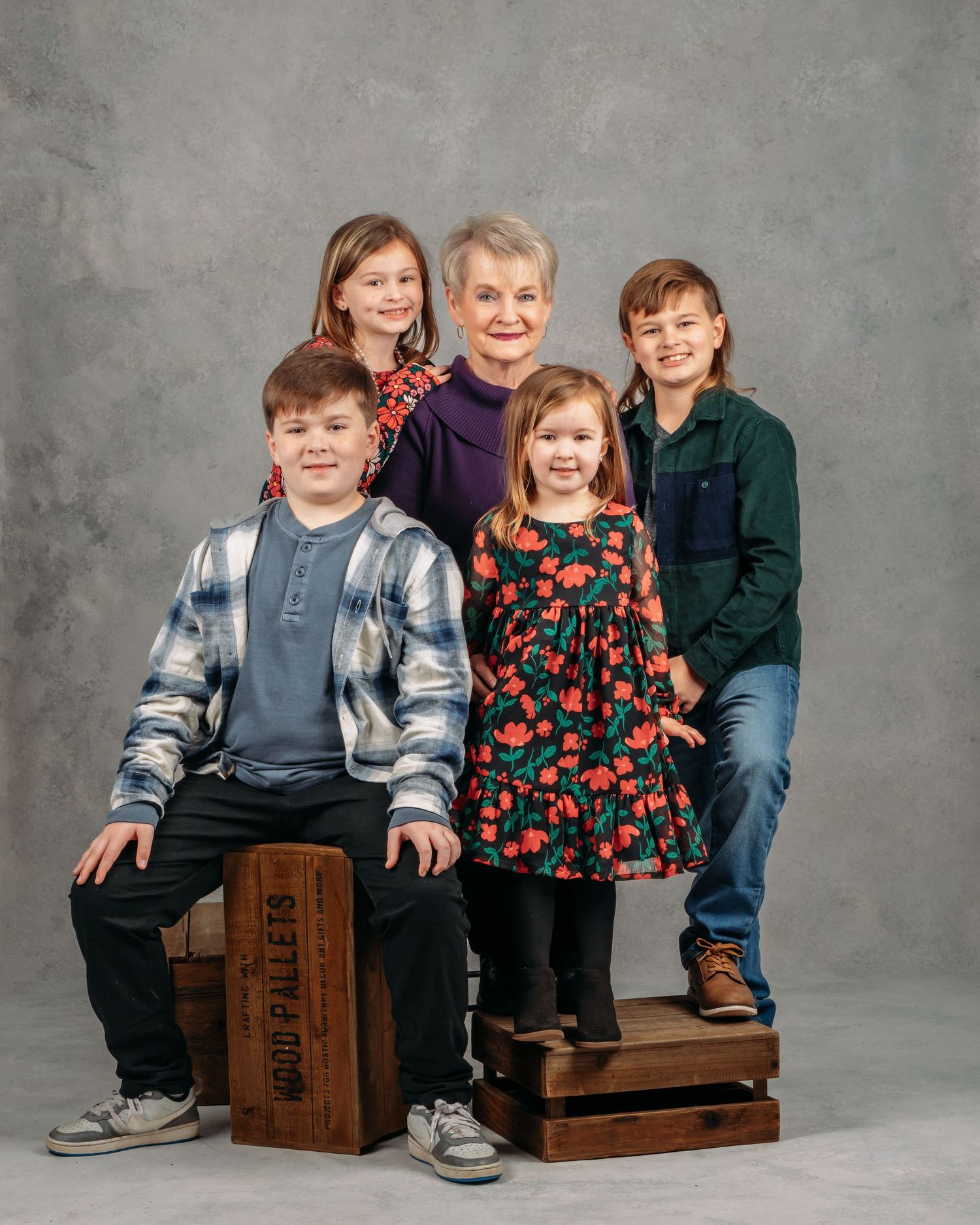 An elderly woman poses with four grandchildren on wooden crates in a studio portrait.