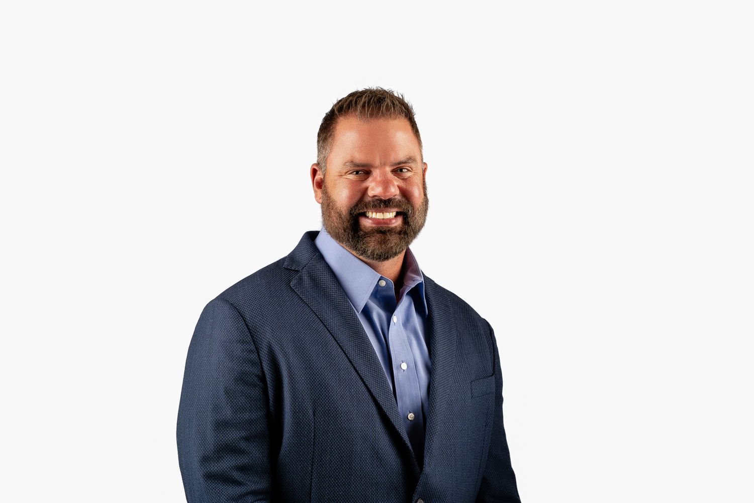 Smiling businessman in navy blazer and blue shirt posing against white background.