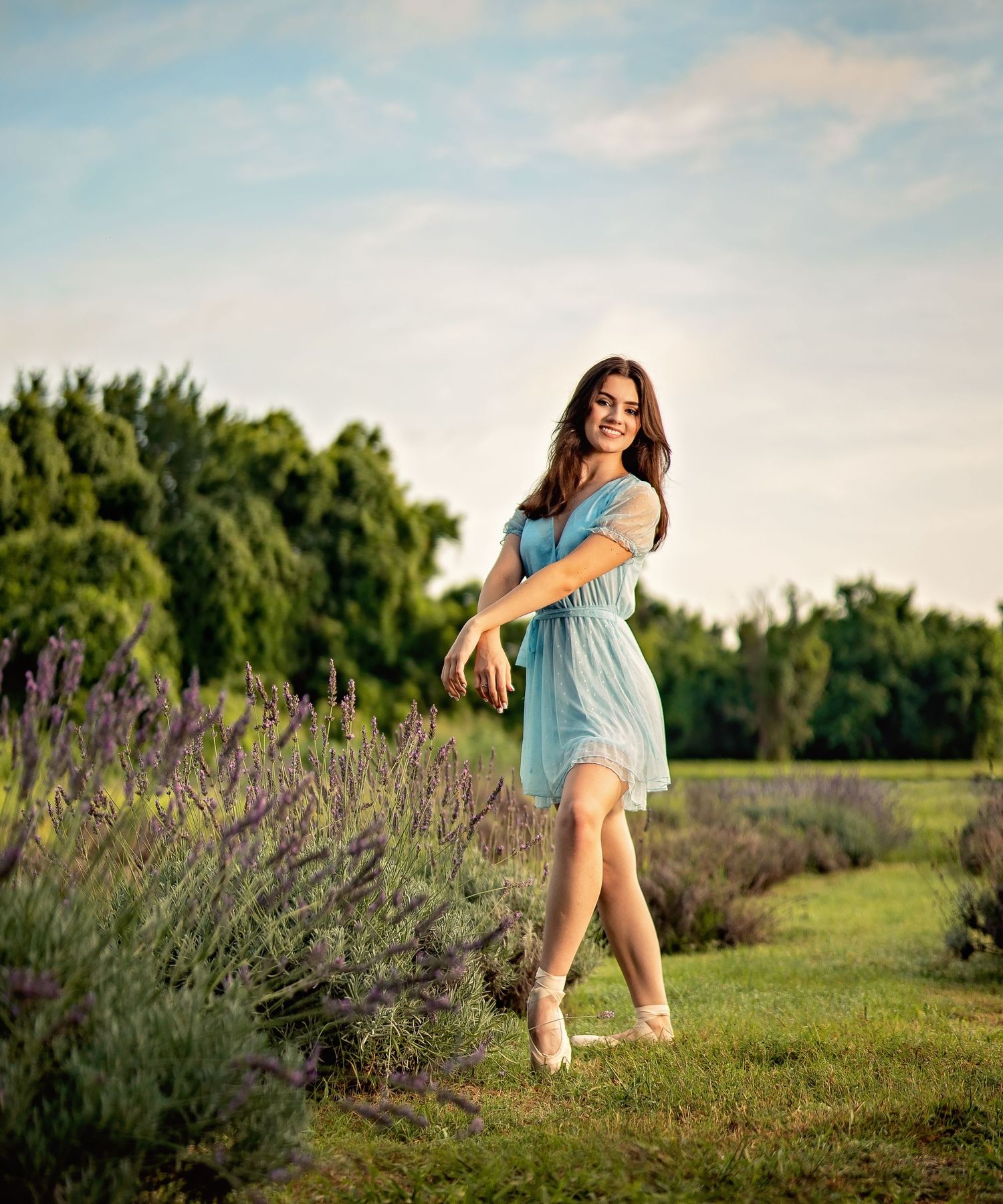 Smiling dancer in blue dress walks through blooming lavender field at sunset.
