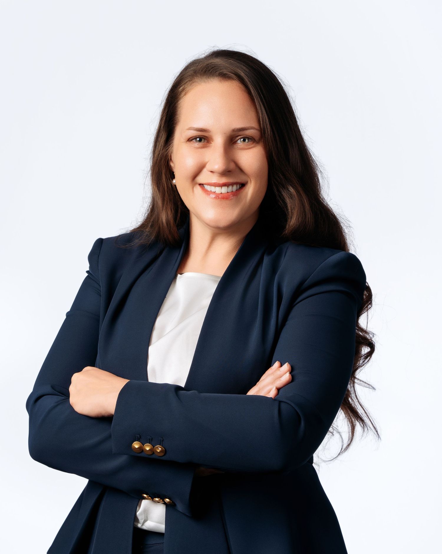 Professional woman in navy blazer smiling with arms crossed against white background.