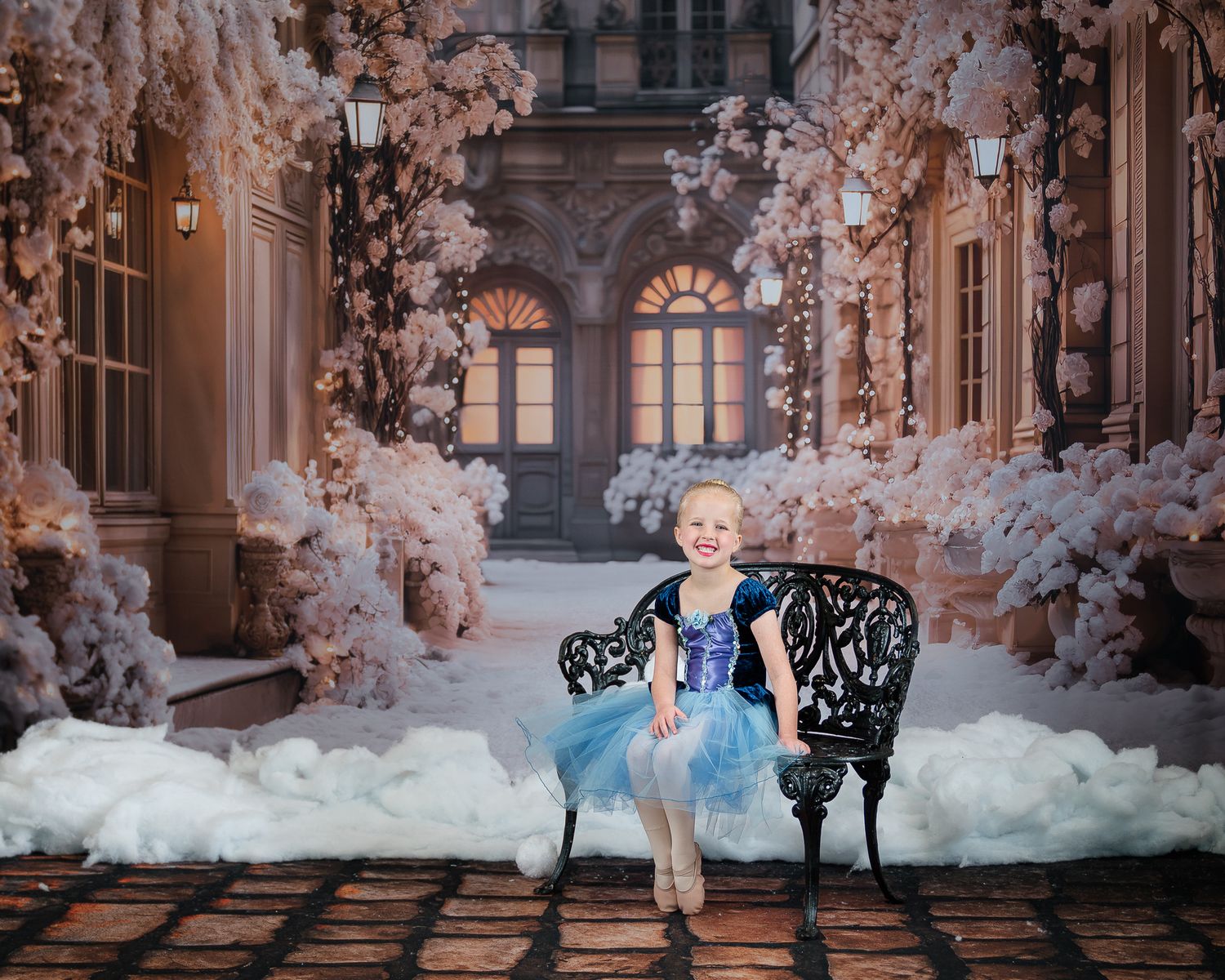 Young girl in blue tulle dress sits on ornate bench with magical winter palace backdrop.
